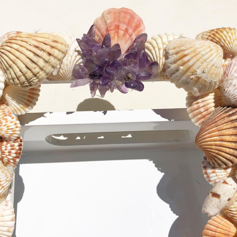 Beautiful found grotto shell photo frame. The frame features several different types of shells and purple gemstones. The frame holds a 5