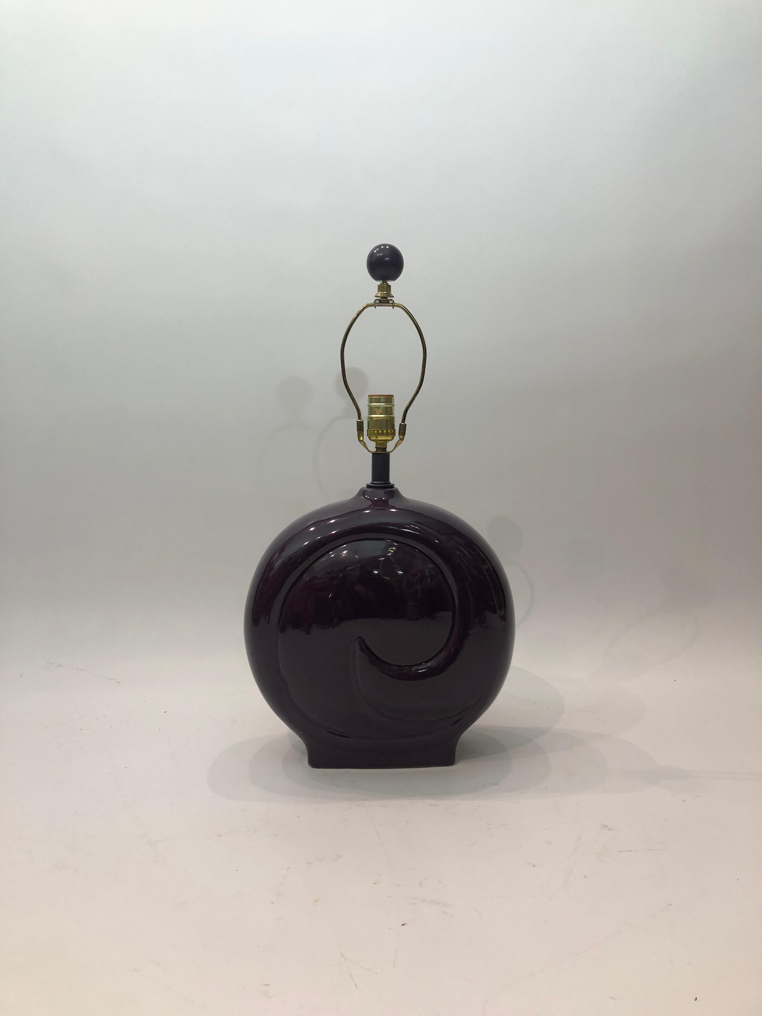 Lámpara de sobremesa de cerámica esmaltada de color morado intenso con un logotipo en relieve similar al de Pierre Cardin. 
Un diseño realmente agradable con un color apagado pero atrevido .
Forma redonda pero bastante estrecha, por lo que encajaría