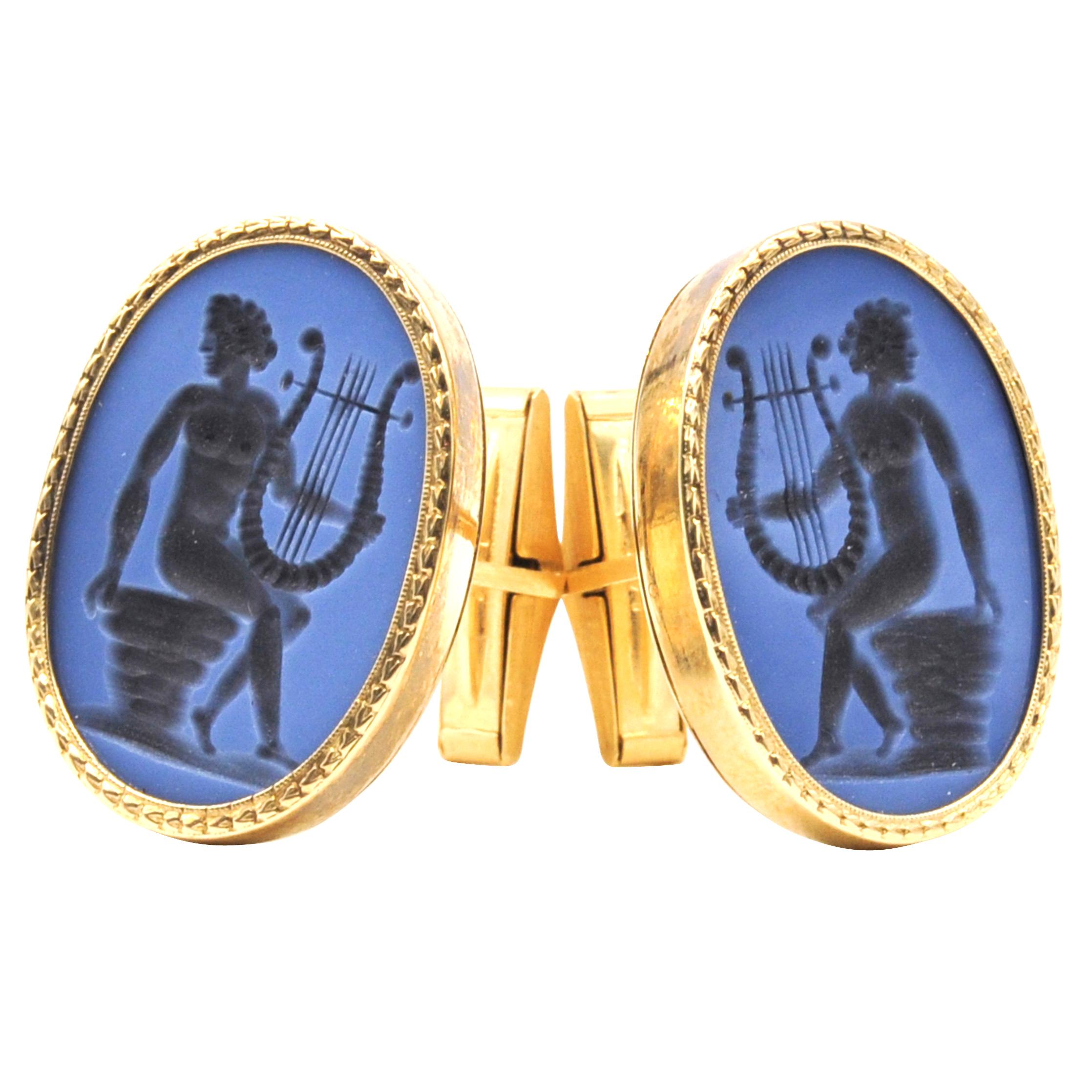 A vintage pair of cuff links crafted in a 14k yellow gold ribbed frame. The pair is set with hand carved Purple Chalcedony intaglio oval shaped gemstones, with angelic harp motifs. This pair is sure to stand out in a crowd. Pair weighs 22.6 Grams.