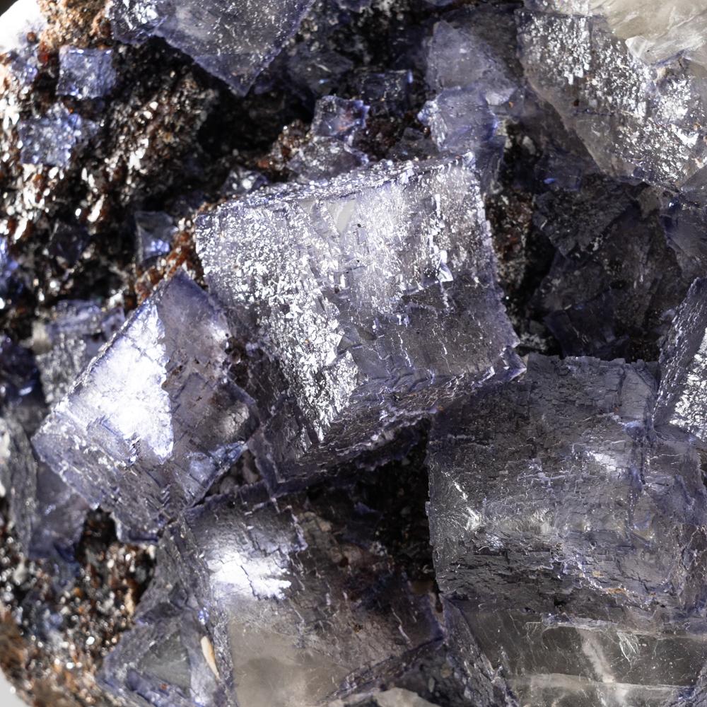 Translucent cubic purple fluorite crystals overgrown on top of a cluster of metallic luster sphalerite crystals. The fluorite surfaces are composed of smaller parallel crystal faces accented by small micro crystal clusters of barite. This