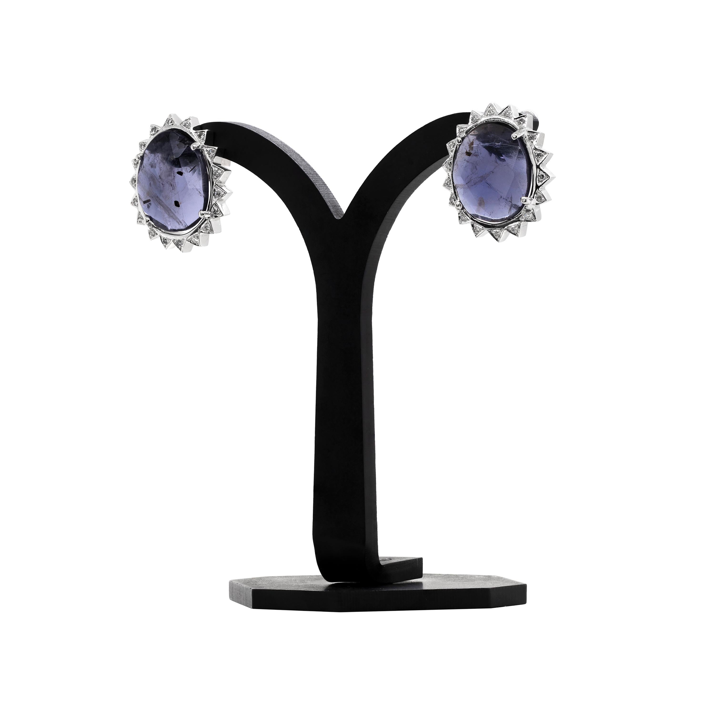 These one of a kind earrings beautifully feature a multi faceted purple iolite stone in the center, weighing approximately 3.70ct in each, mounted in a four claw, open back setting. The iolite is wonderfully surrounded by 18 round brilliant cut