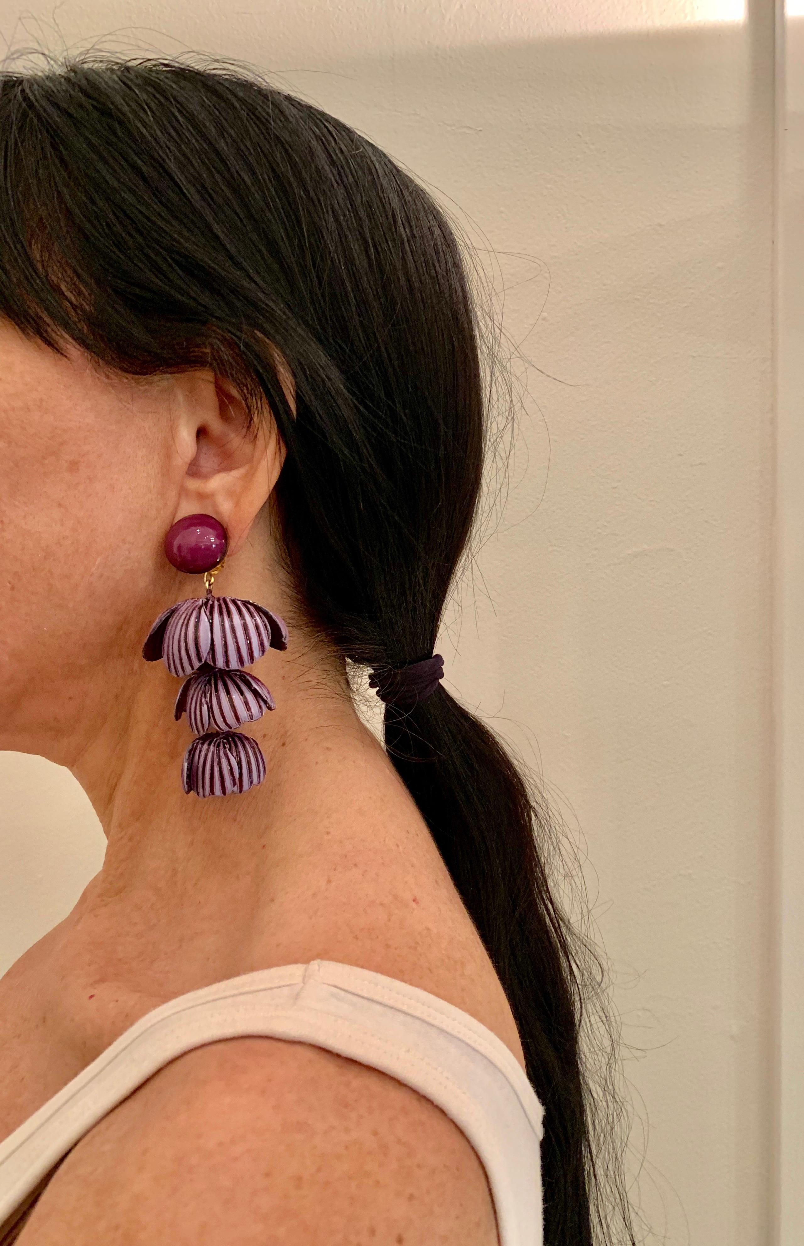 Light and easy to wear, these handmade artisanal contemporary clip-on earrings were made in Paris by Cilea. The lightweight statement earrings feature three rows of architectural enameline (enamel and resin composite) purple flower petals. The