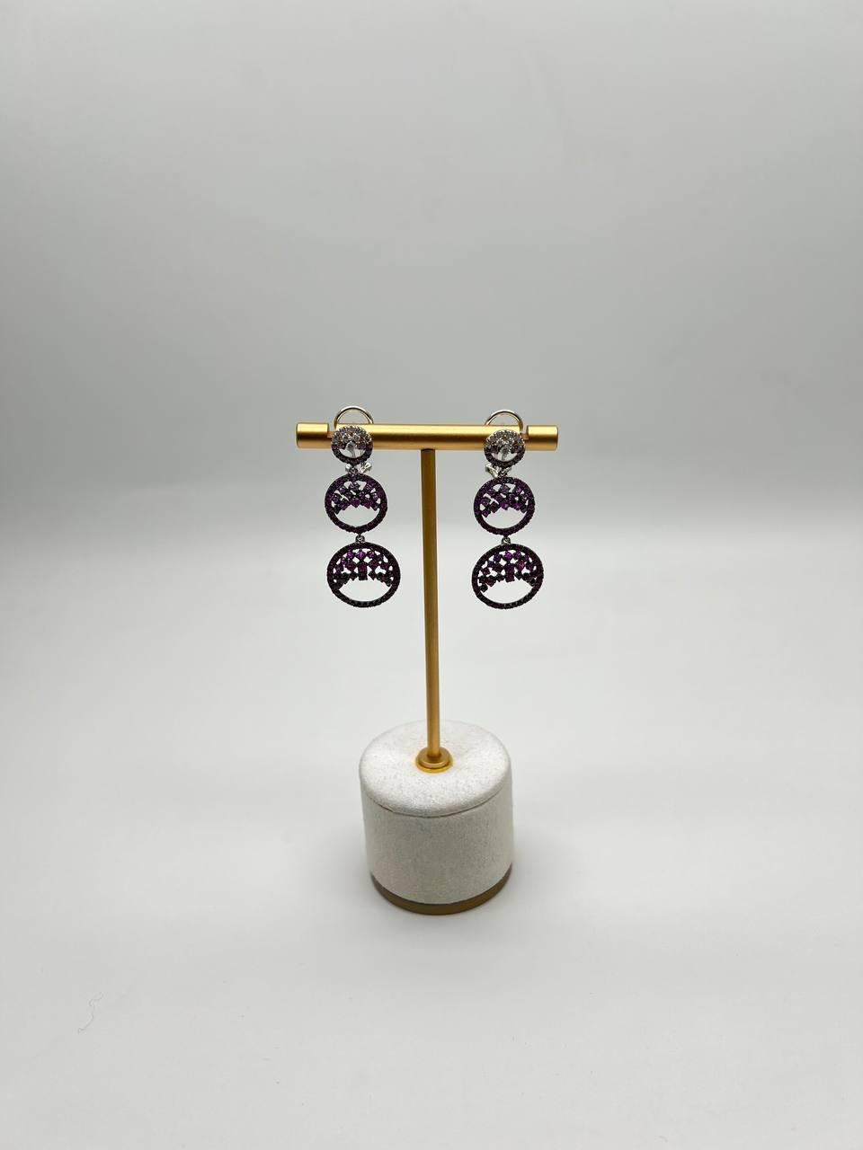 Elevate your style with these stunning dangle earrings.

Crafted with intricate circular designs, each piece features a captivating array of purple and pink sapphires and white diamonds, creating a striking visual contrast.