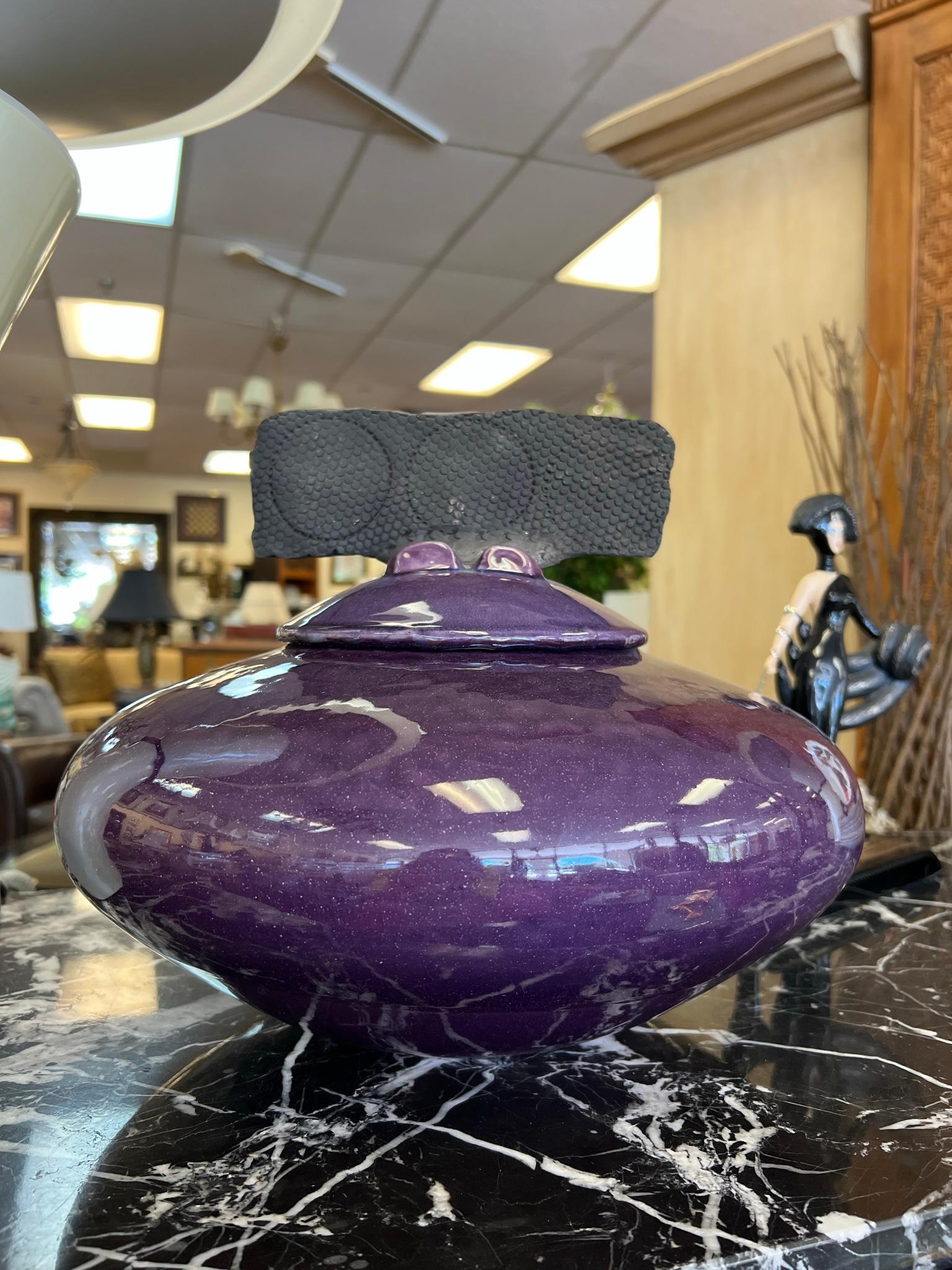 A striking example of contemporary Raku pottery, this artisan-crafted lidded terrine by M. Hines showcases the depth and individuality inherent in this centuries-old ceramic tradition. The piece is rendered in a rich, purple glaze, with subtle tonal