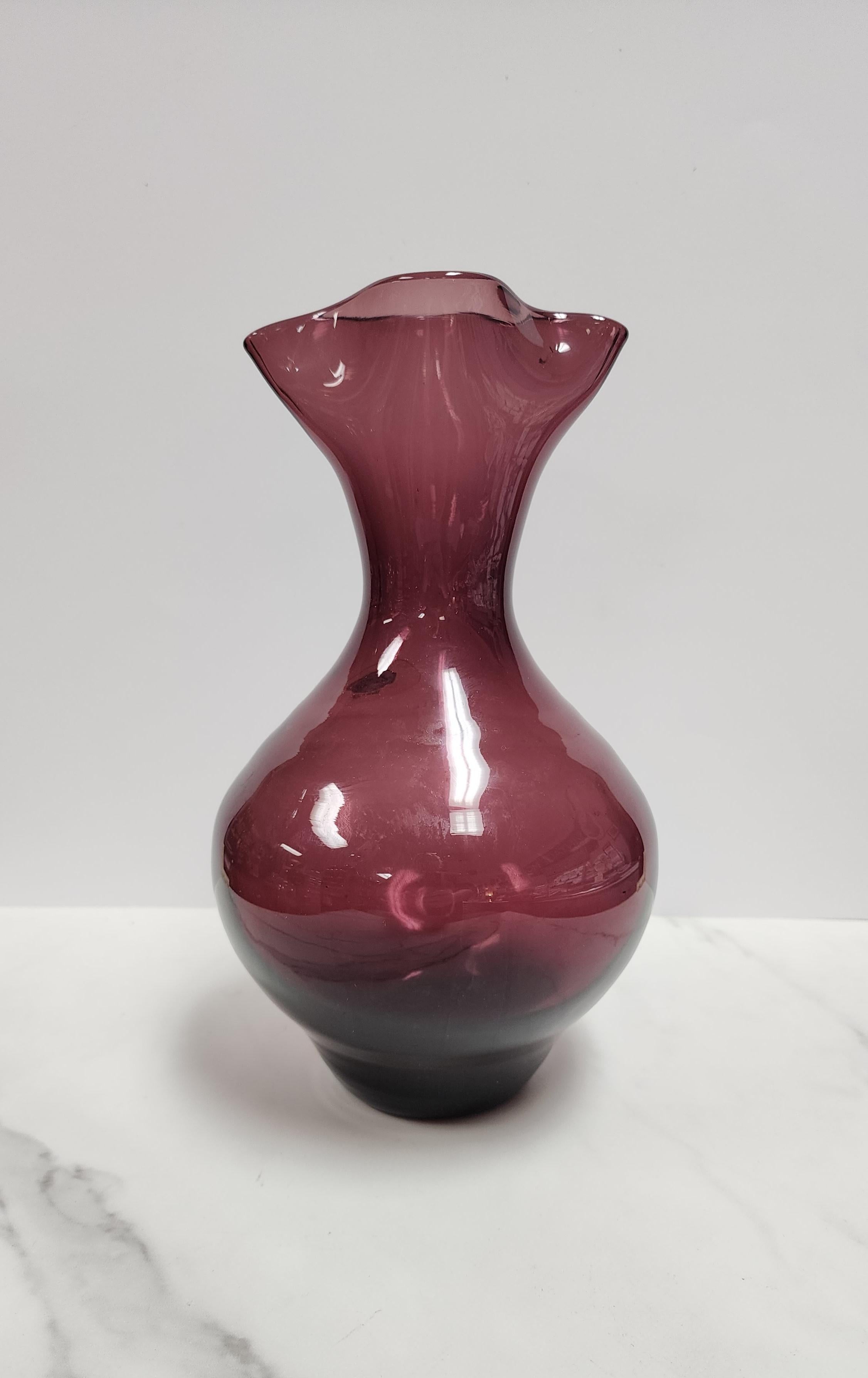 This Blenko amethyst vase is signed on the bottom and still has the original foil tag. The bottom is marked Retro Blenko 2002 and is signed by the artist. It has the pinched spout and is in excellent condition. 
This vase is a gorgeous purple that