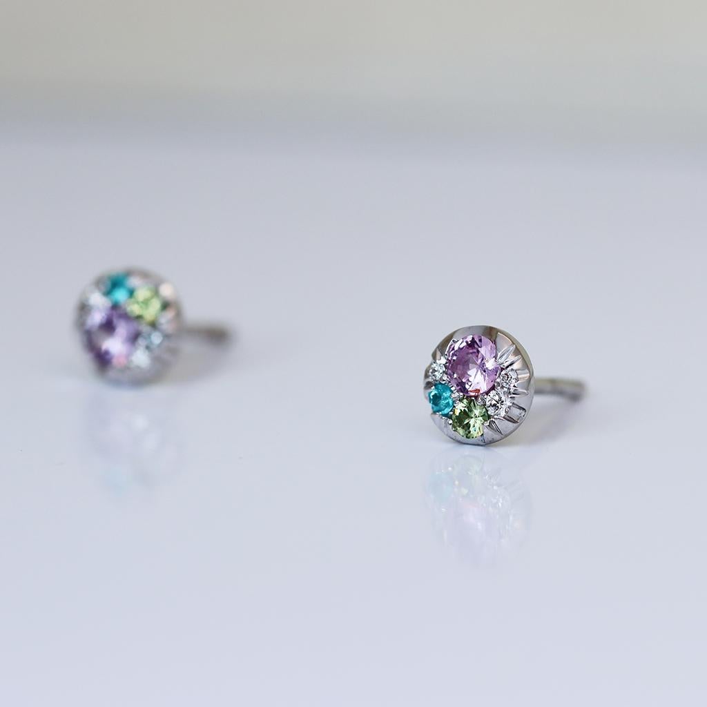 Handmade in Belgium by jewellery artist Joke Quick, with no casting or printing involved, these earrings are truly one of a kind. 

These tiny white gold stud earrings display mesmerizing purple sapphires, Paraïba tourmalines from Brazil, demantoid