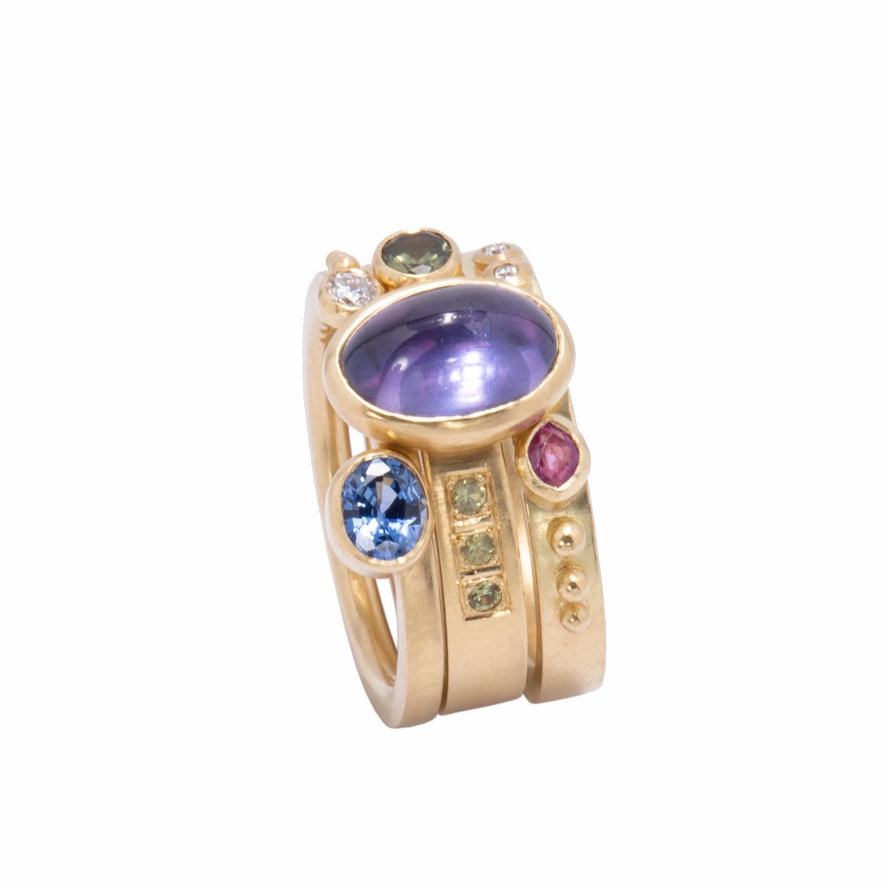 Colored sapphires in pink, blue and green, a demantoid garnet and diamonds orbit an oval purple sapphire cabochon 3.59cts in our Purple Sapphire Stack Ring Set handcrafted in 18k gold with our signature satin finish. A narrow band and 2 wider bands