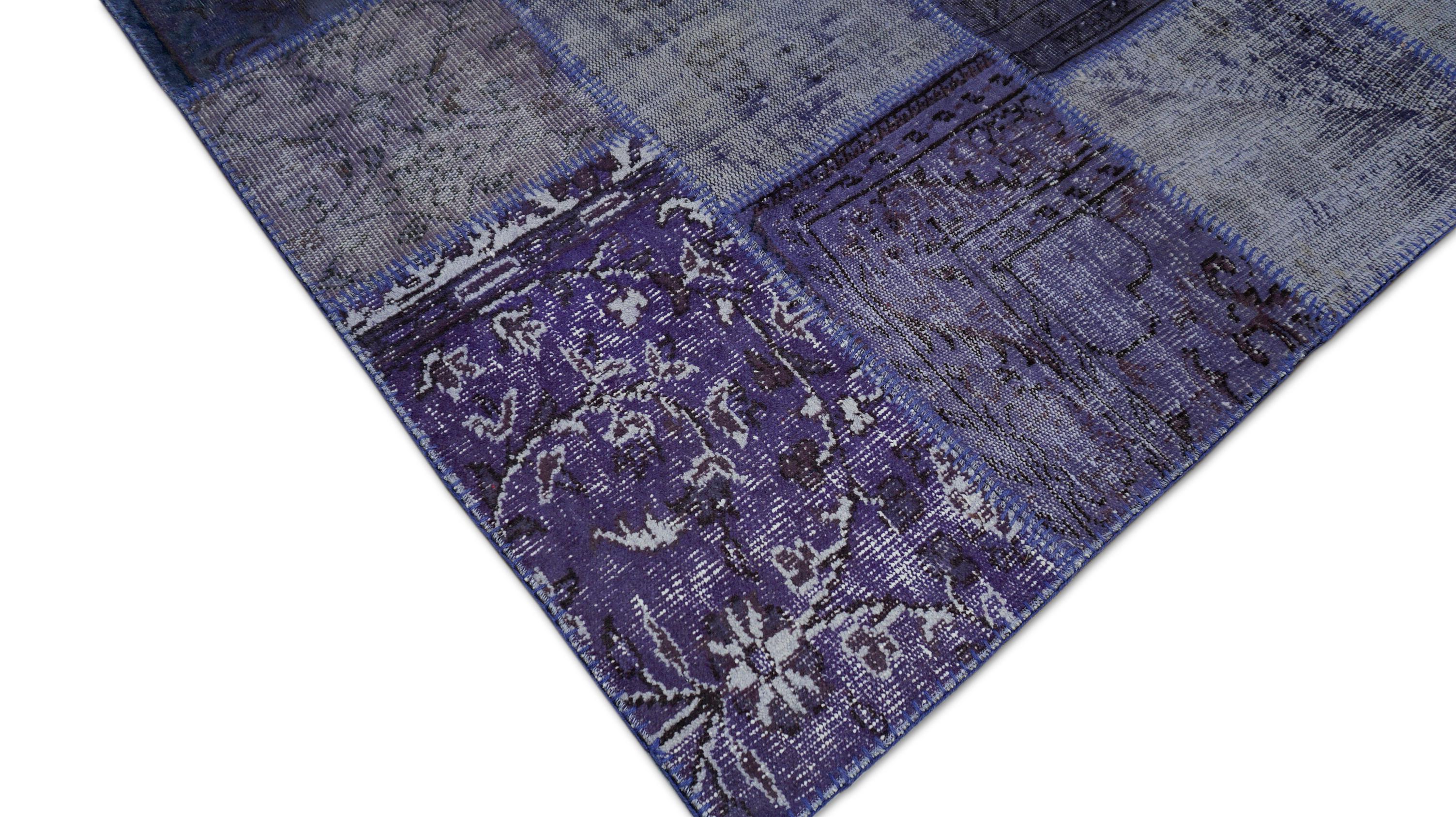 Dieser handgewebte Wollteppich ist eine kühne und zeitgemäße Interpretation traditioneller Textilkunst. Er zeigt ein lebendiges Patchwork aus Vintage-Teppichfragmenten, die in satten Lila-, Weiß- und Anthrazittönen gefärbt sind. Der Teppich