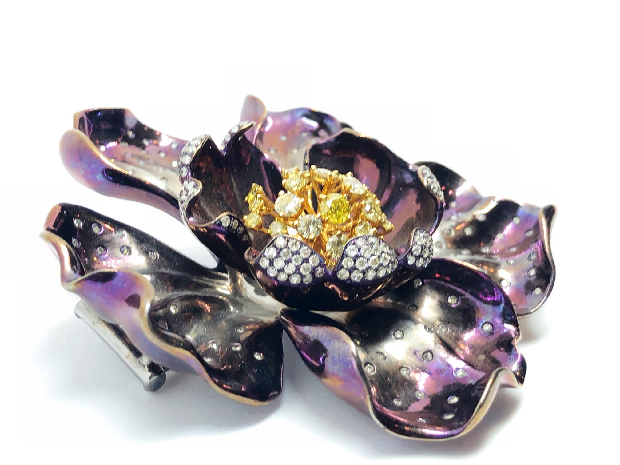 A purple flower brooch, mounted in titanium, with five shaded purple to silver outer petals set with round brilliant-cut diamonds, and three inner petals set with round brilliant-cut diamonds on the edges of each petal, with white and yellow