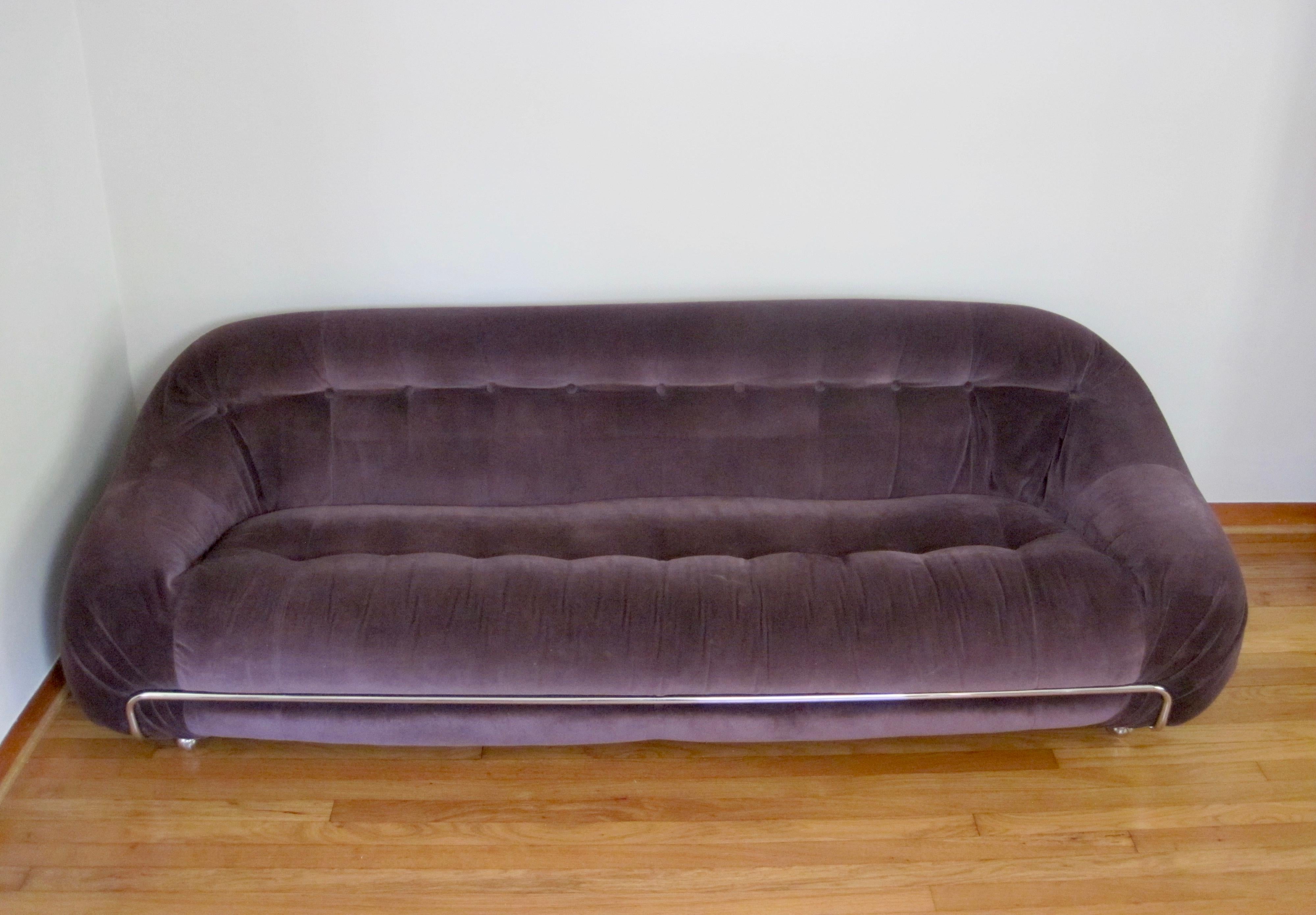 A purple velvet low profile sofa in the manner of Tobia Scarpa Soriana. 
This sofa sits low and is comfortable, cushioned yet firm.
Tufted on the seat and back, pleated at ends where back meets arms. A chrome bar across the front adds more detail.