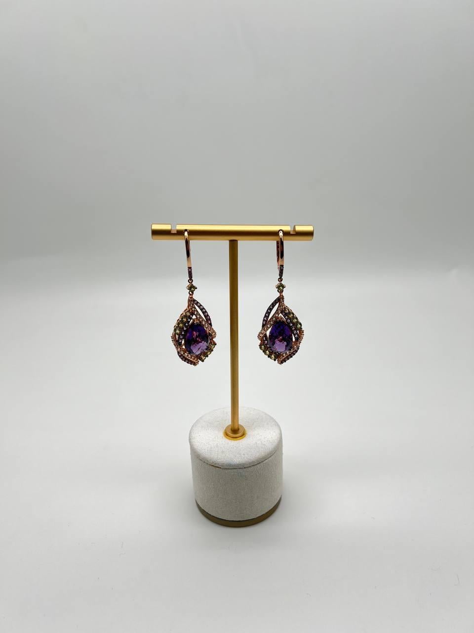 Exquisite dangle earrings featuring a captivating teardrop amethyst. Central amethyst stones are encircled by intricate layers of sparkling diamonds, creating a mesmerizing play of color and light. The earrings are suspended from a delicate