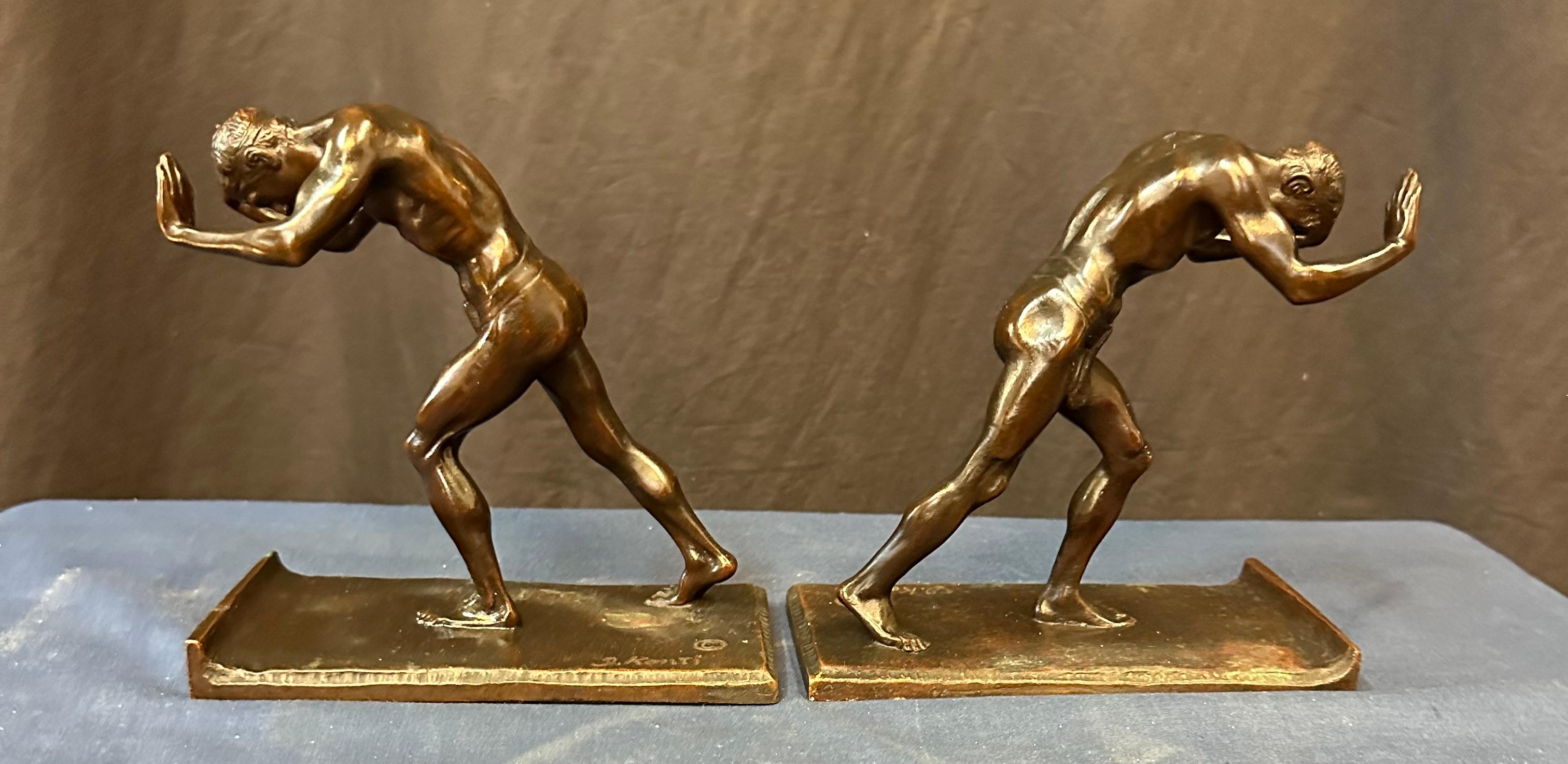Cette paire vintage de serre-livres Art of Vintage en bronze patiné date du début du 20e siècle. Le sculpteur Isidor Konti a magistralement créé cette paire de jeunes hommes musclés partiellement nus, uniquement vêtus d'une étoffe de pagne. Chacune