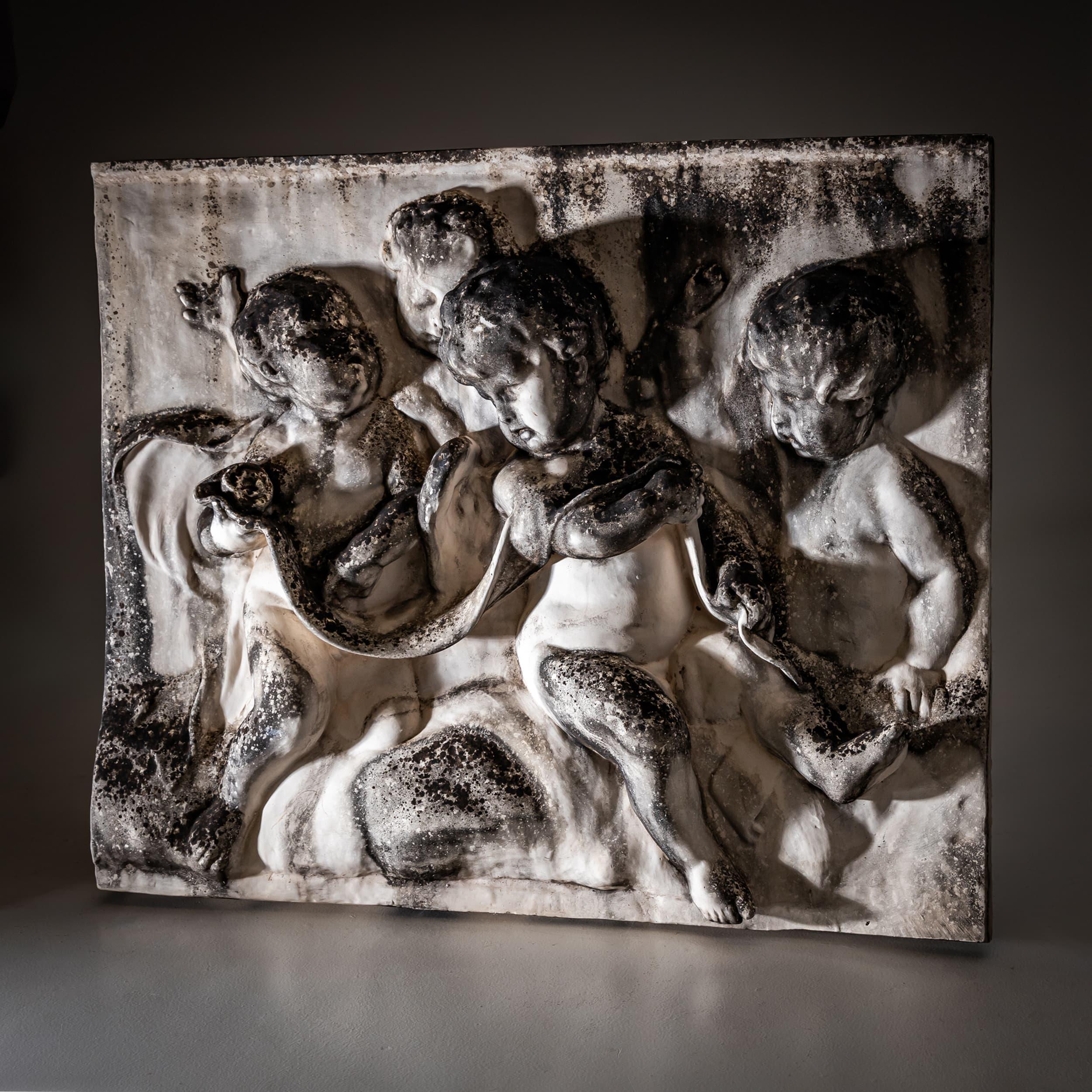Rectangular relief crafted from white biscuit porcelain, depicting four playful putti in dynamic poses. A flowing drapery and entwined snake link the figures compositionally. The surface features age-related patina and discolorations, enhancing the