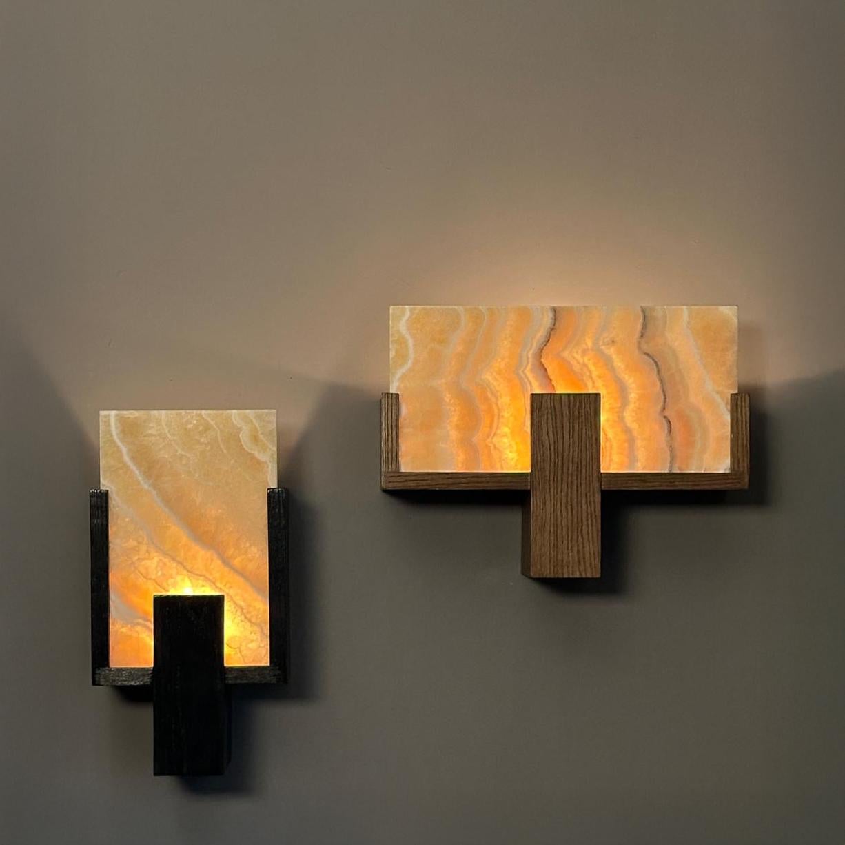 Un'applique da parete dalla semplicità audace e forte. Il paralume è disponibile in Alabastro, per una luce calda e dorata, o in marmo turco di Carrara per un look più elegante e moderno. La struttura è realizzata in rovere massiccio, disponibile