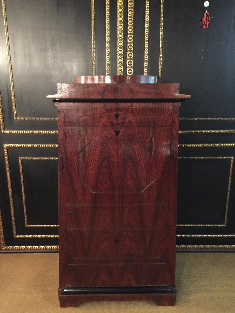 Fine armoire pyramidale dans le style Biedermeier.
Placage acajou de haute qualité sur bois tendre massif. Corps conique sur base de cadre profilé. A l'avant, grande porte centrale avec placage pyramidal en acajou, derrière laquelle se trouvent des