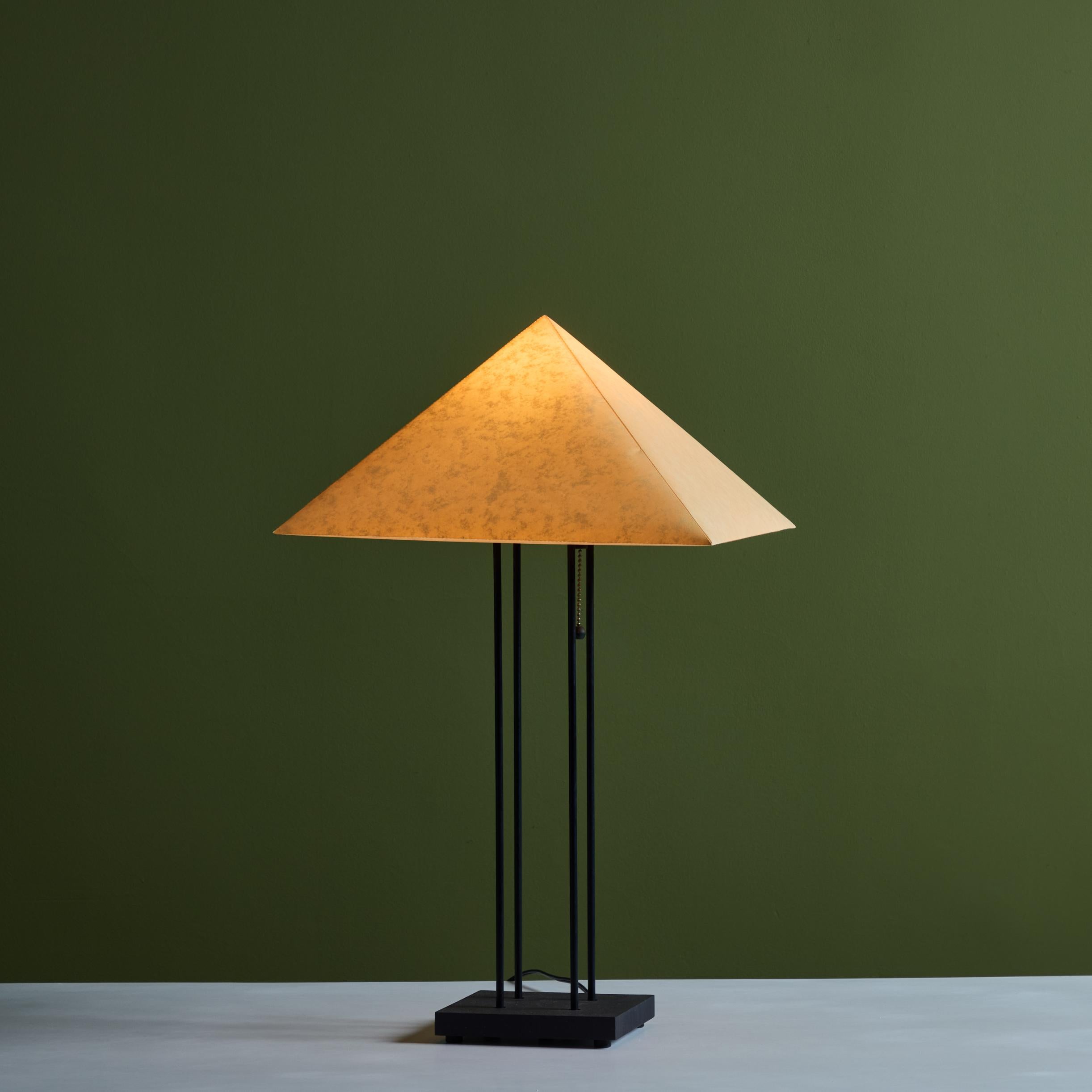 Lampe de table postmoderne avec abat-jour en papier et corps émaillé noir. La tige de la lampe comporte quatre tiges sur une base carrée, avec un abat-jour en papier en forme de pyramide. La lampe est munie d'une chaîne de traction qui permet de