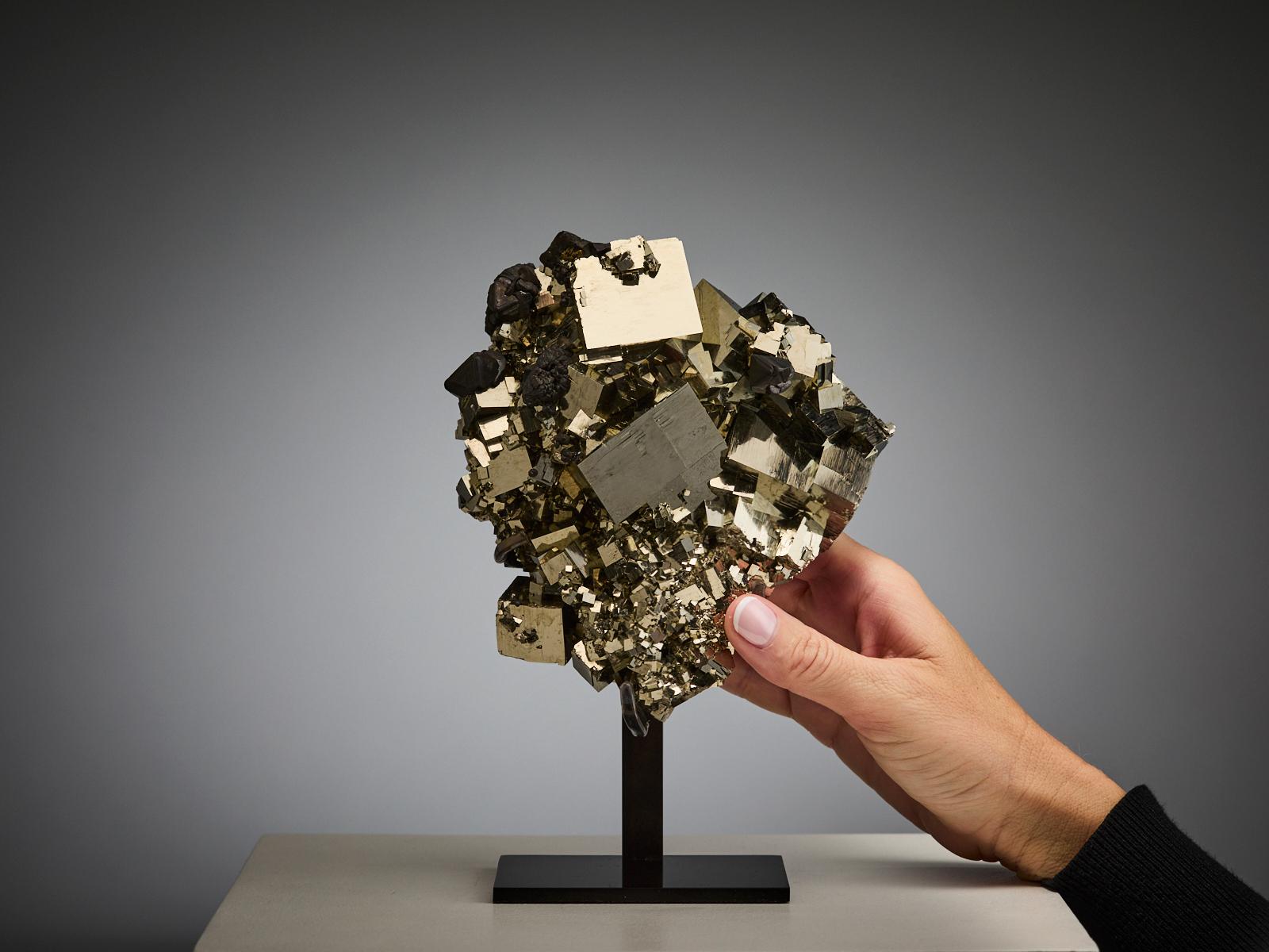 An extraordinary pyrite cluster from Peru, composed of intergrown golden cubes of different sizes, all perfectly arranged to form a striking and sculptural piece. Some areas display touches of dark hematite, creating a beautiful contrast against the