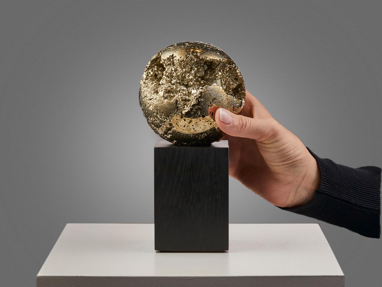 This beautiful pyrite sphere from Peru shines with a golden metallic
surface and has crystals of different sizes all around it. Some parts of the
sphere are open, allowing you to look inside and see even more crystals
growing toward the center. It’s
