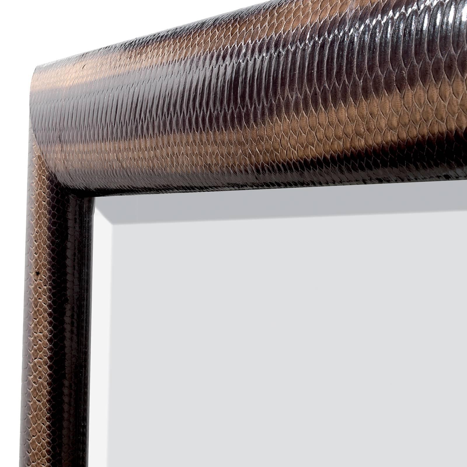 Part of the Python collection, featuring striking mirrors whose elegant frames are upholstered in genuine python leather, this piece features a wooden structure and back. The mirror, with minimalist moldings at the edges, is enclosed in a stunning