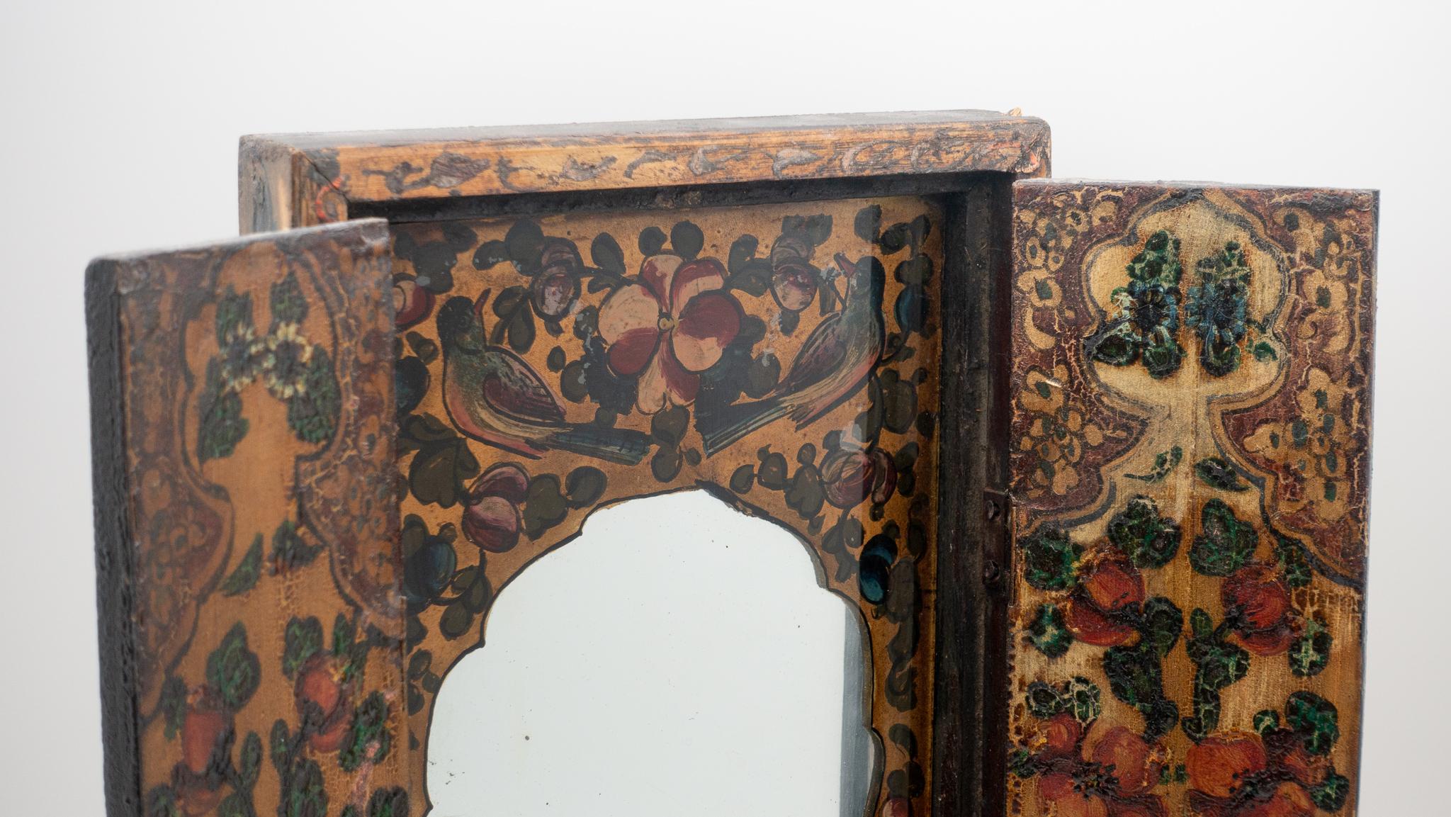 19th century Qajar-era Persian mirror with painted wood frame, hinged panels that open to reveal a painted églomisé mirror interior, and a wooden back cover to protect the glass.