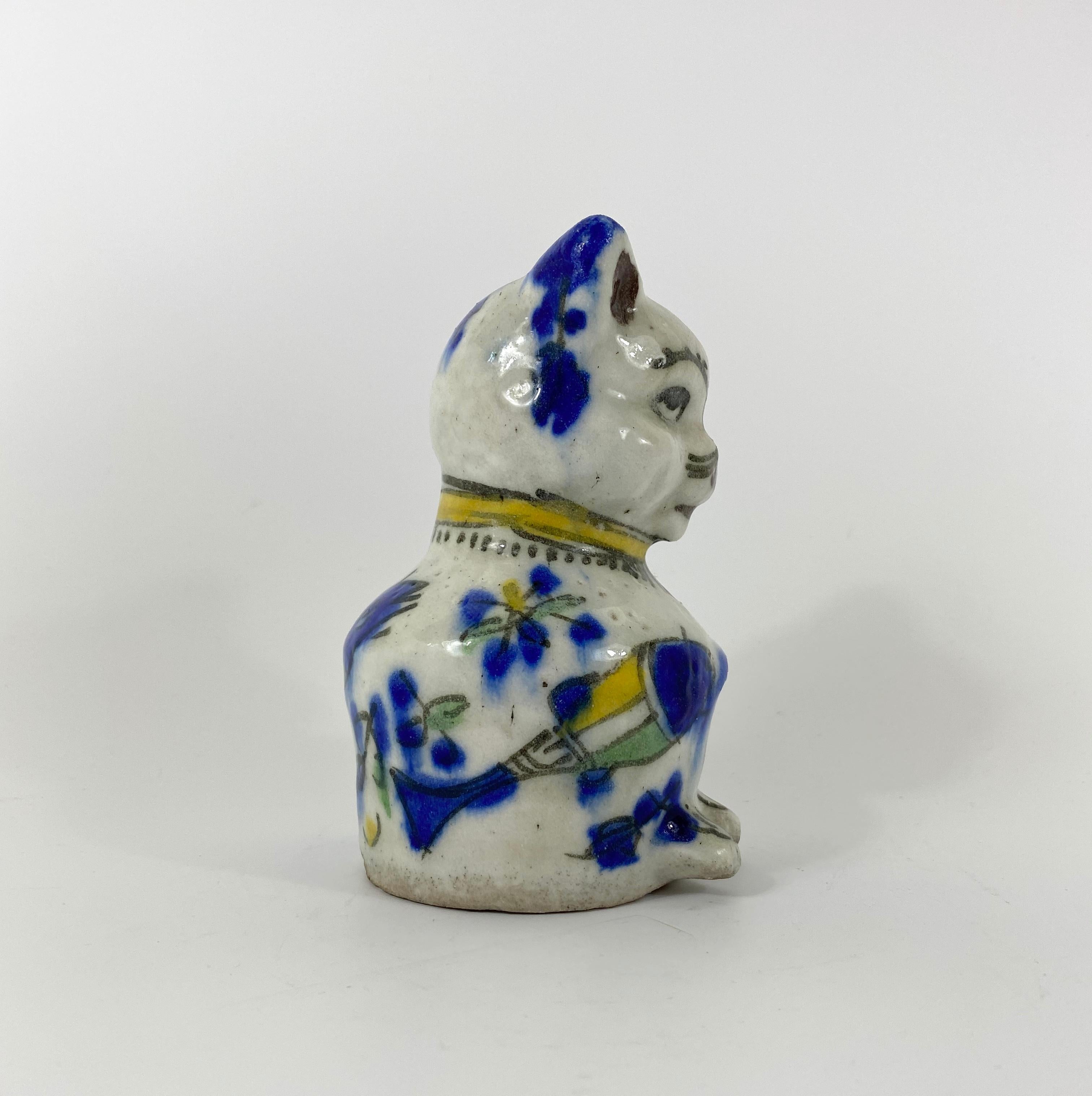 A Qajar pottery cat, Iran, circa 1880. The chubby seated cat, painted to the body with two large fish, a bird and an insect in underglaze enamels. The cat wears a yellow collar, and it’s moulded tail sweeps around to under its chin.
Measures: