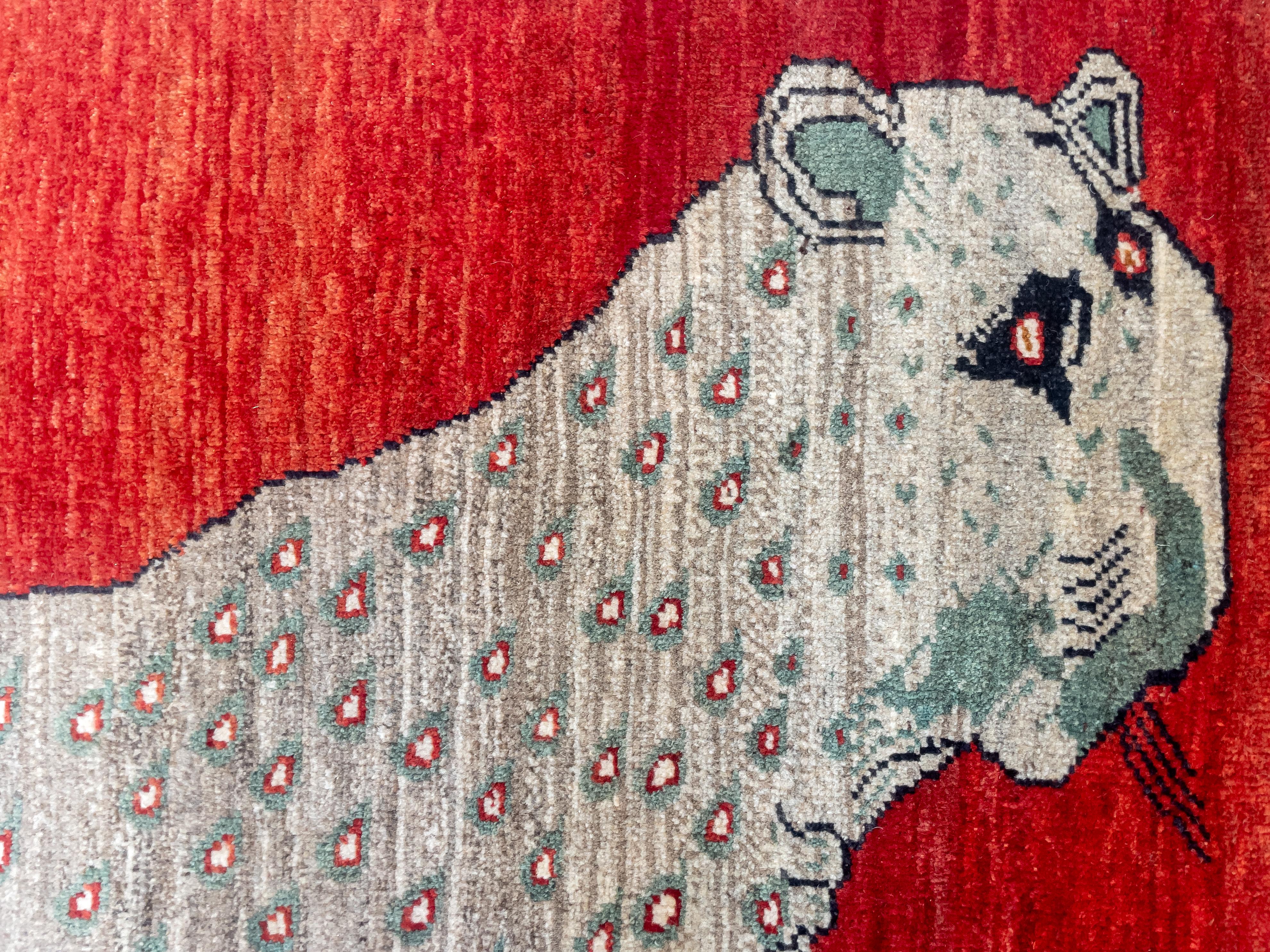 Questo tappeto persiano Qashqai in lana vintage misura 5' x 7' e presenta un'impressionante figura di leopardo in grigio e verde su uno sfondo rosso. Annodato a mano da abili artigiani tessitori in lana su un ordito e una trama di lana, la maestria