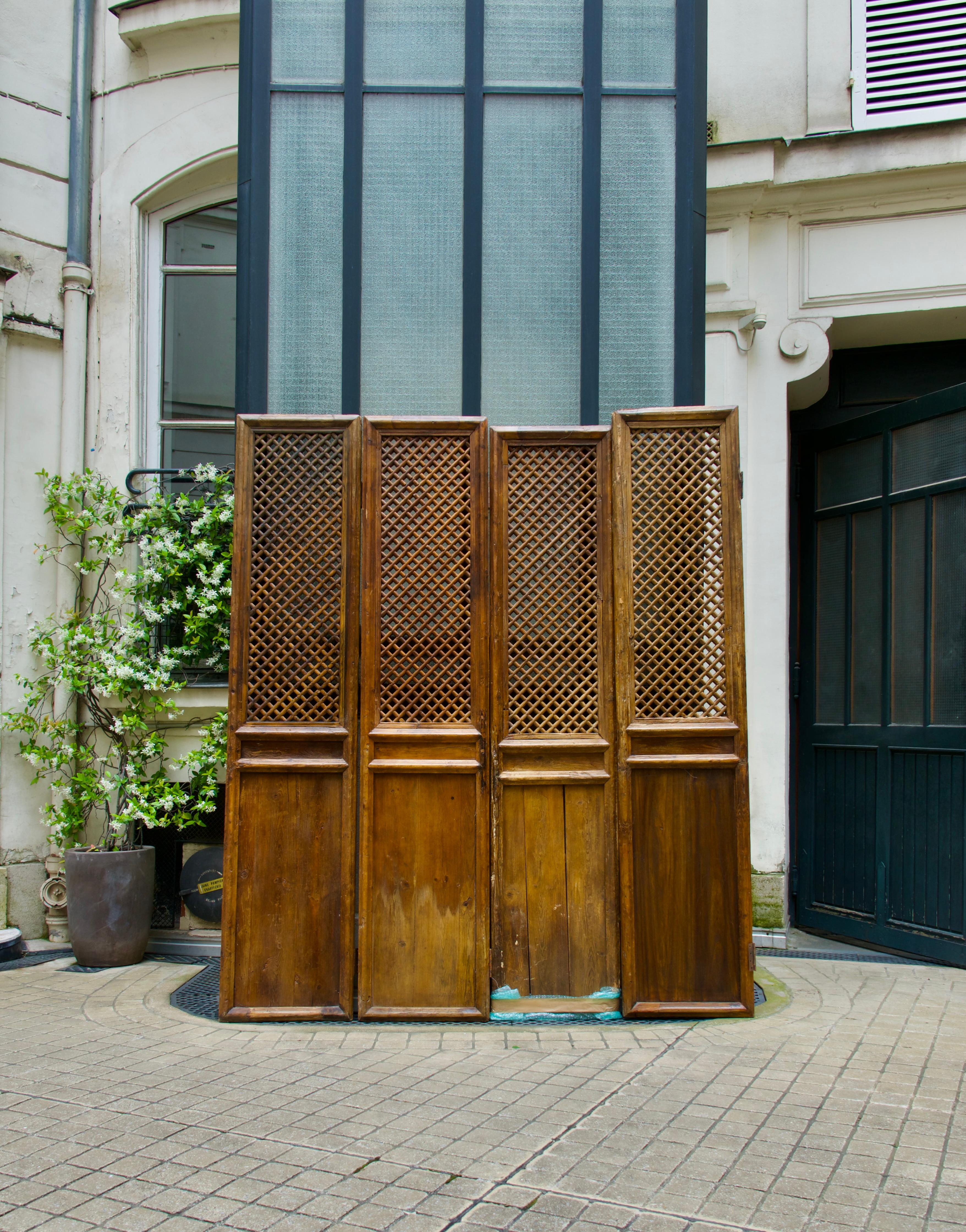 Set of four patinated wooden doors or lattice partitions, China, early 20th century. Rectangular in shape, with solid lower sections and open latticework in the upper sections, some with remaining hinges (some rusted). Originally sliding doors,