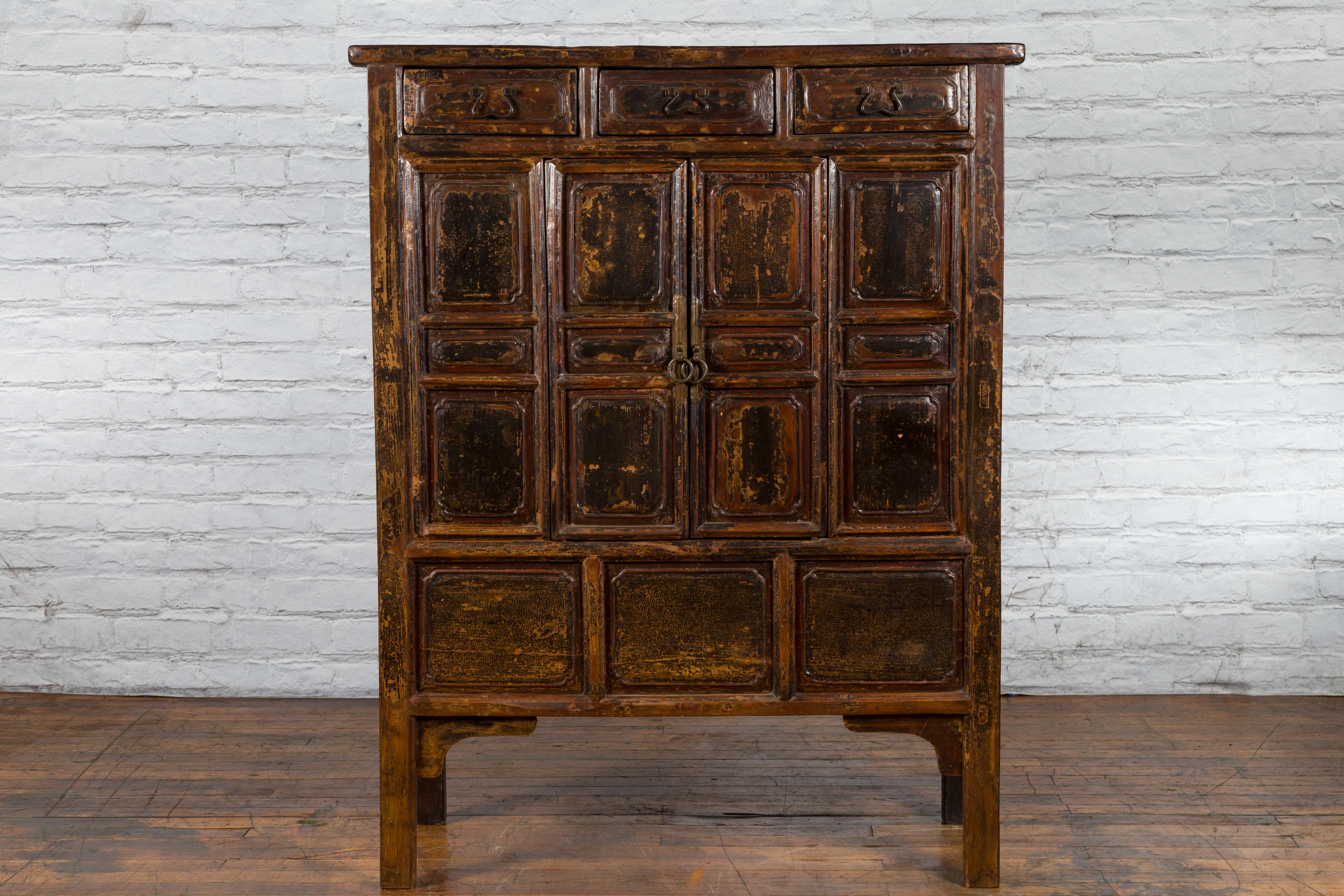 A dark brown lacquered Qing Dynasty Chinese cabinet from the early 19th century with three drawers, double doors and nicely distressed patina. Created in China during the early years of the 19th century, this hand carved cabinet features three