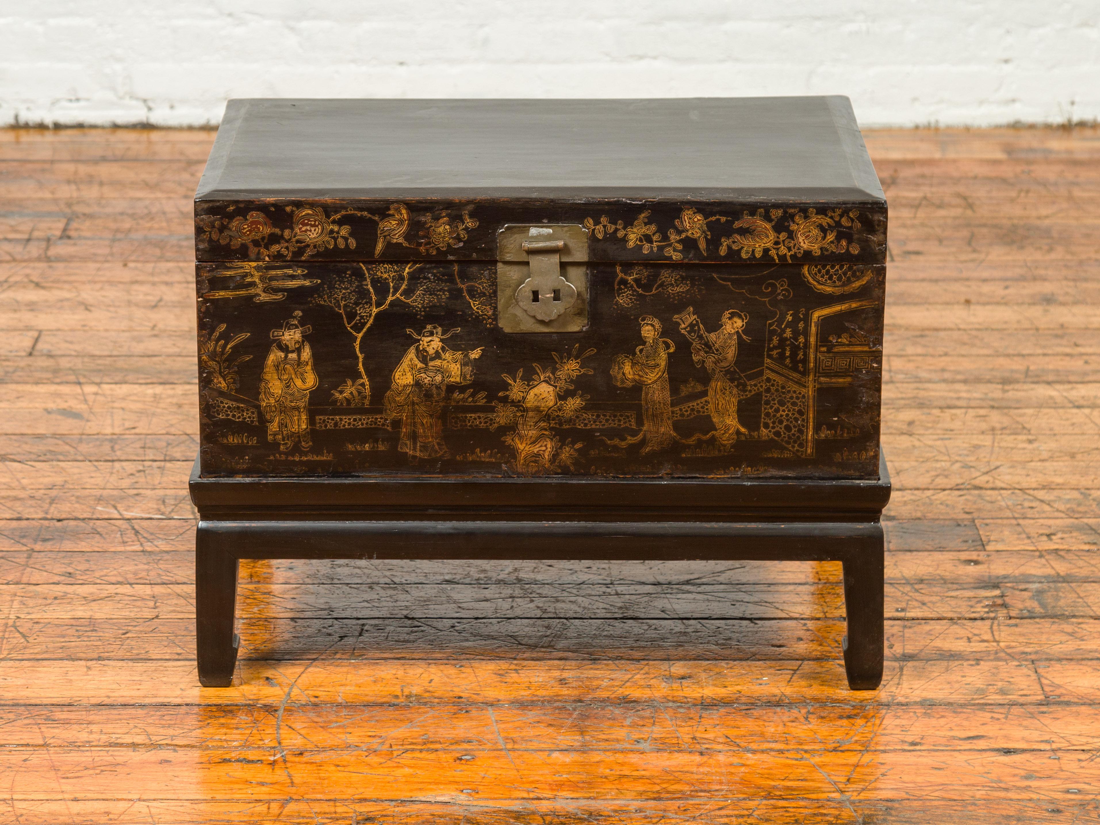 A Chinese Qing Dynasty blanket chest on base from the 19th century, with chinoiserie painting on the front. Crafted in China during the Qing Dynasty, this black and gold chest features a rectangular lid with slightly beveled edges, that opens thanks