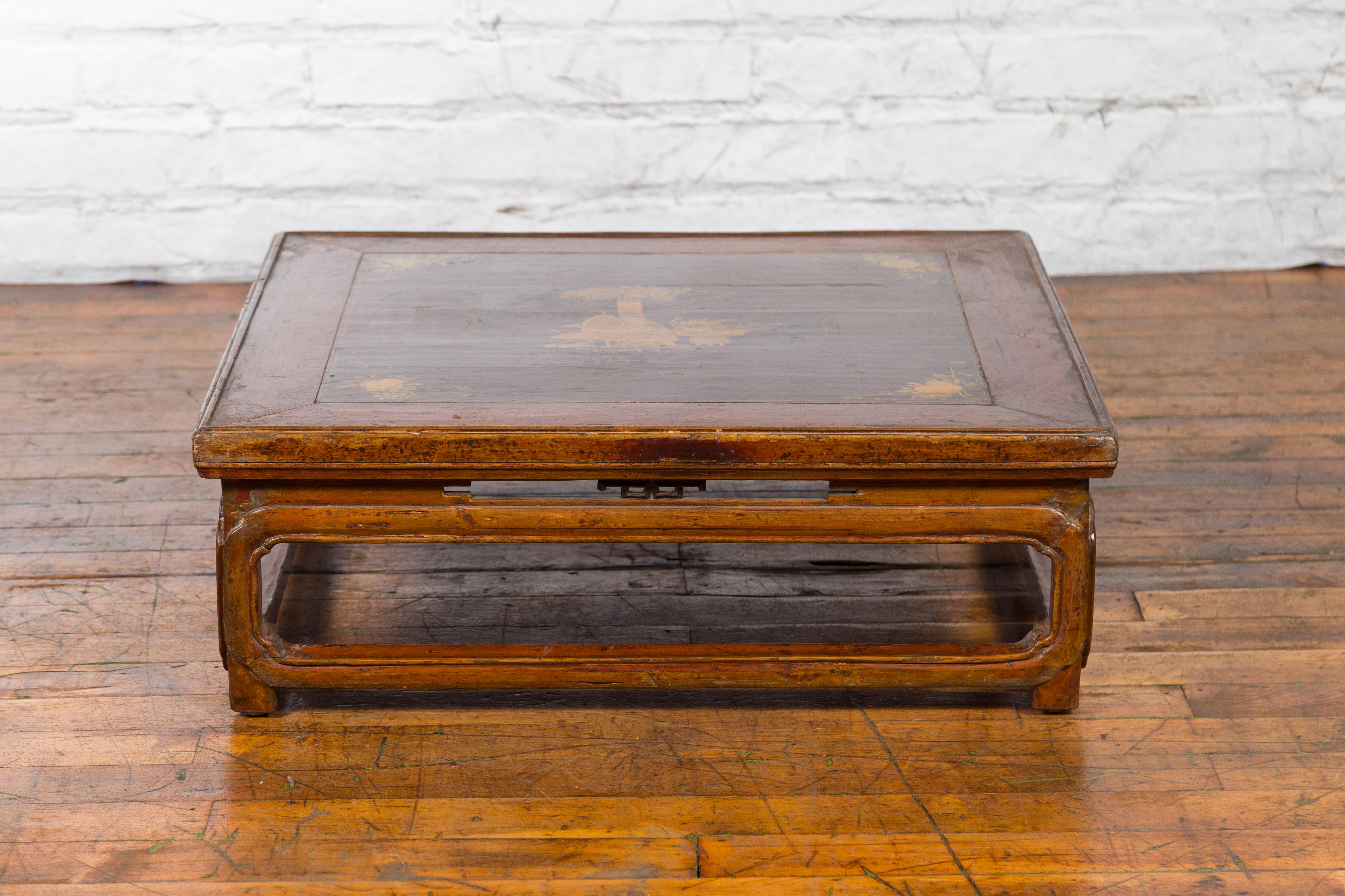 A Chinese Qing Dynasty period low kang coffee table from the 19th century, with painted décor and pierced apron. Created in China during the Qing Dynasty, this low kang coffee table features a square top adorned on its central board with a painted