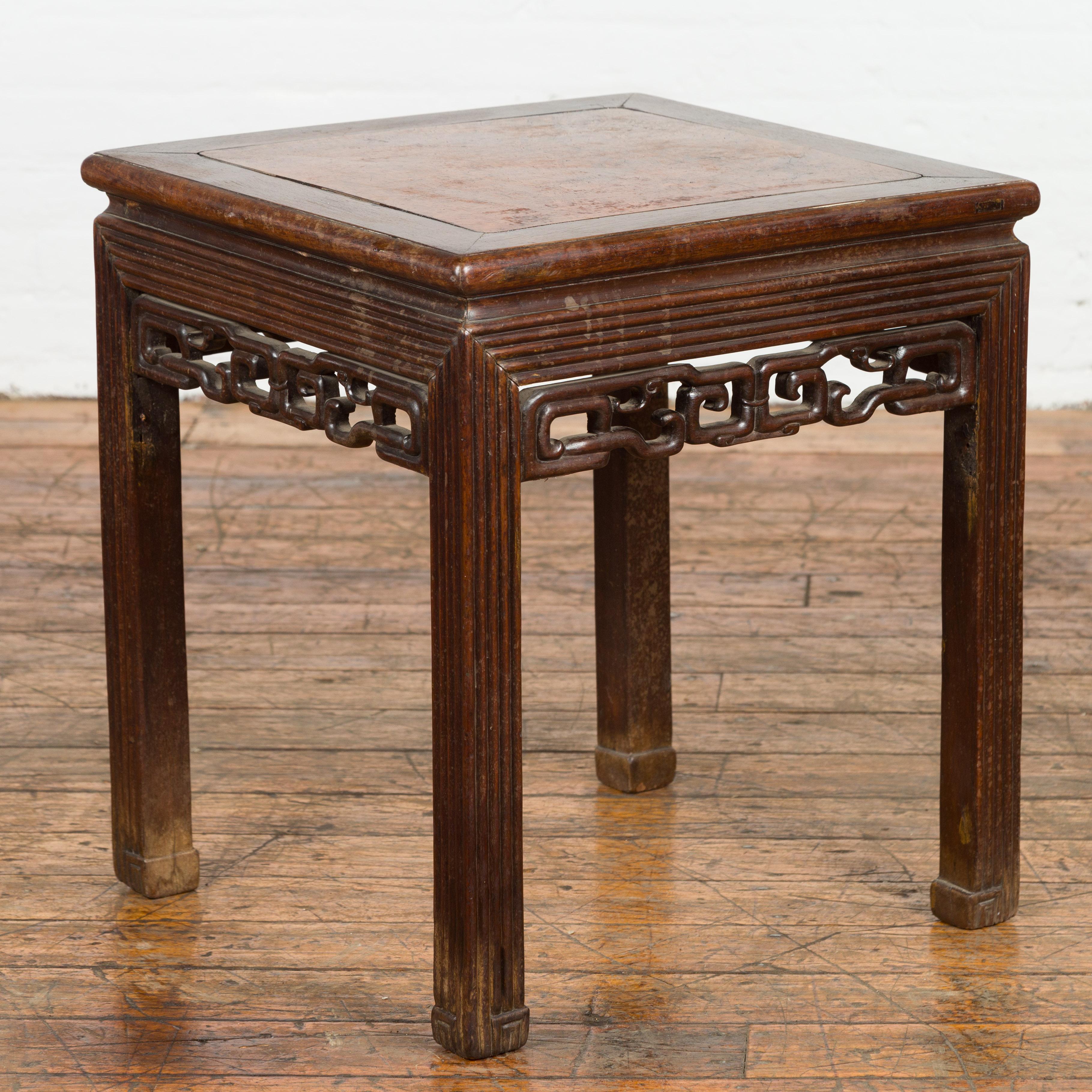 A Chinese Qing Dynasty period side table from the 19th century with inset burl top, carved reeded base and fretwork motifs on the apron. Behold a piece from the esteemed Qing Dynasty period – this Chinese side table is a harmonious symphony of