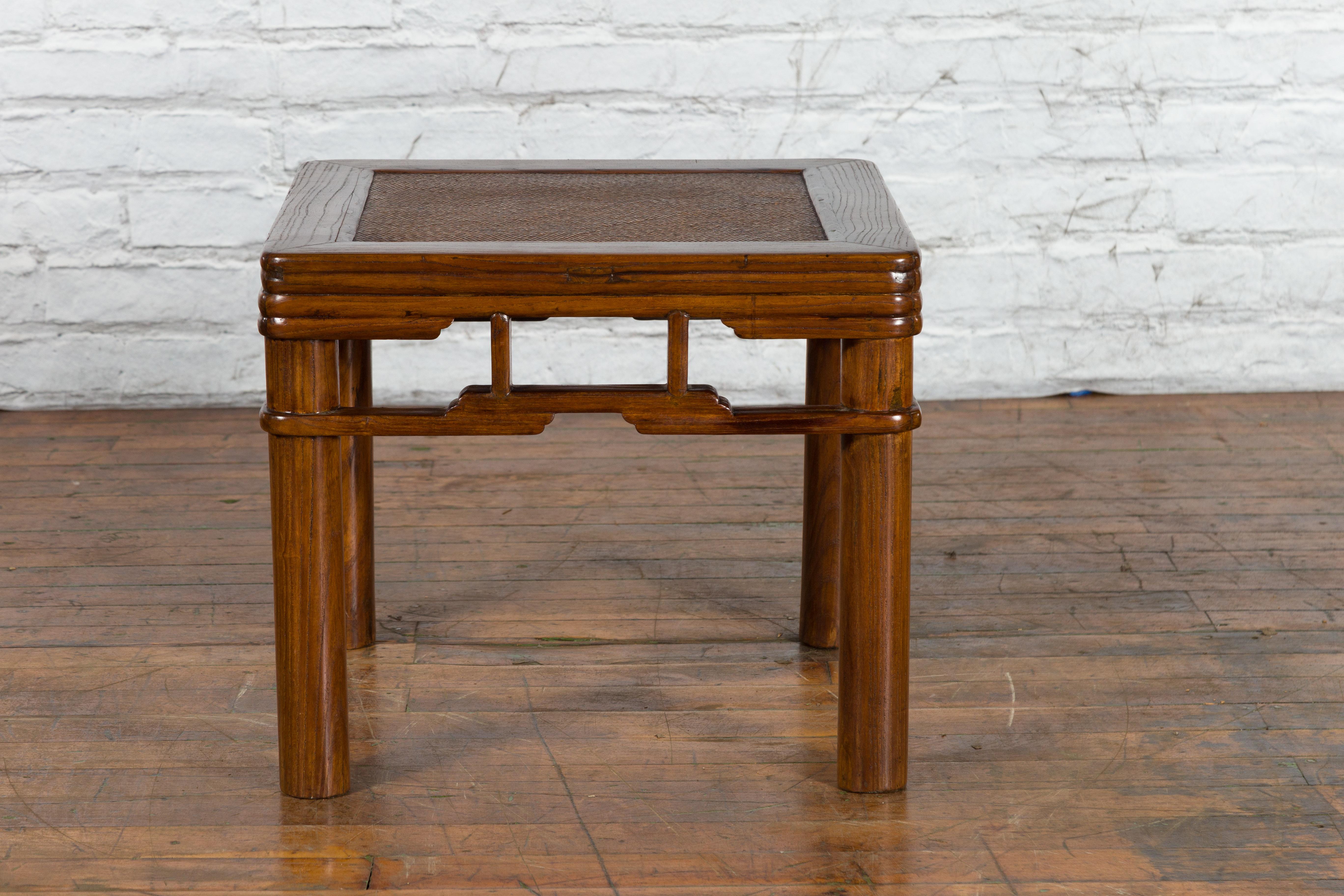 A Chinese Qing Dynasty period wooden side table from the 19th century, with rattan top and pillar strut motifs. Created in China during the Qing Dynasty, this wooden side table features a square top with rattan inset, sitting above a reeded apron