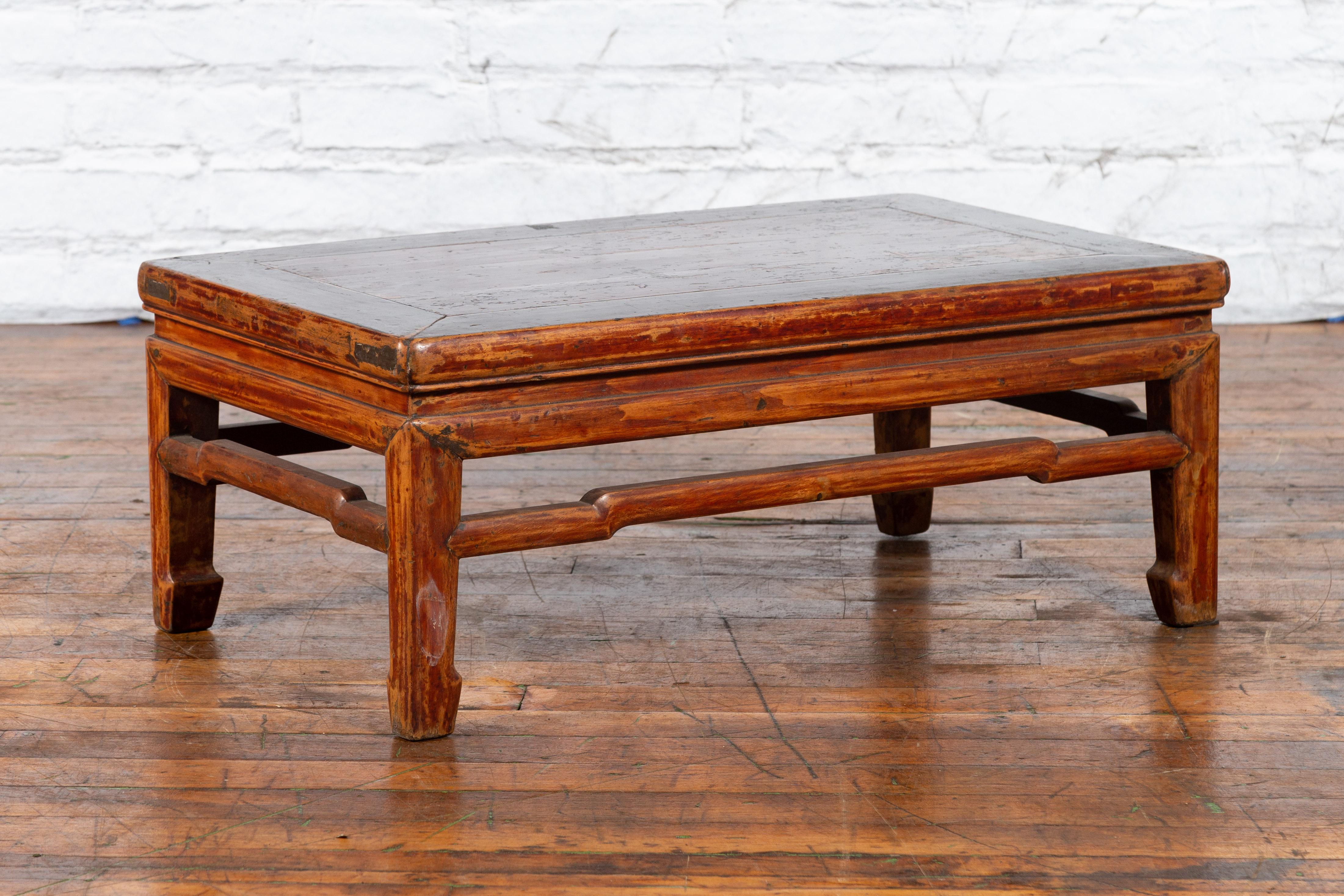 A Chinese Qing Dynasty period distressed low table from the 19th century with humpback stretchers and horse hoof feet. Created in China during the Qing Dynasty period, this low table features a rectangular top with central board, sitting above a