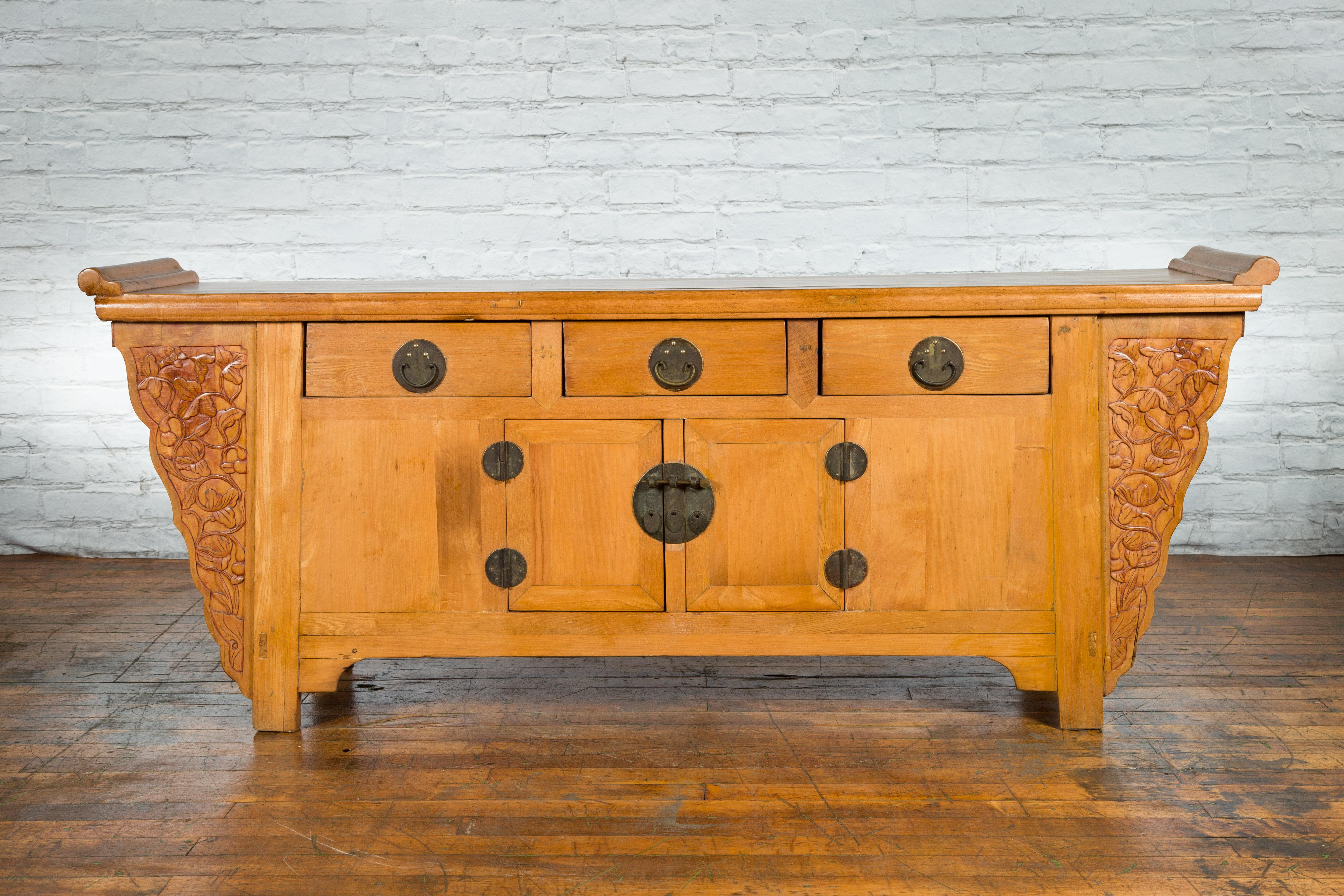 A Chinese Qing Dynasty period sideboard from the 19th century, with natural finish, carved spandrels and everted flanges. Created in China during the Qing Dynasty, this large sideboard features a rectangular planked top flanked with everted flanges,