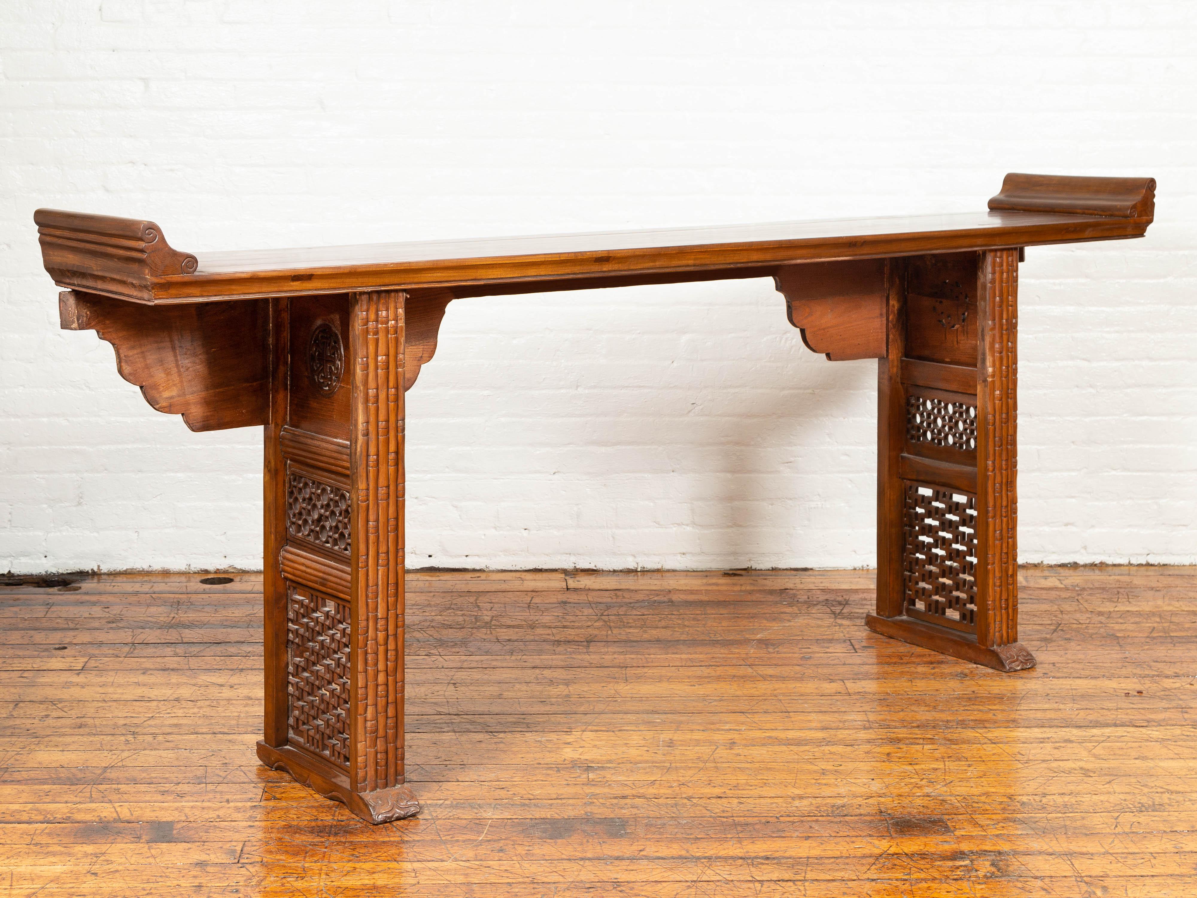 A Chinese Qing dynasty period altar console table from the early 20th century, with everted flanges, hand carved bamboo style design and fretwork motifs. Born in China during the Qing dynasty, this altar console table features a rectangular top,