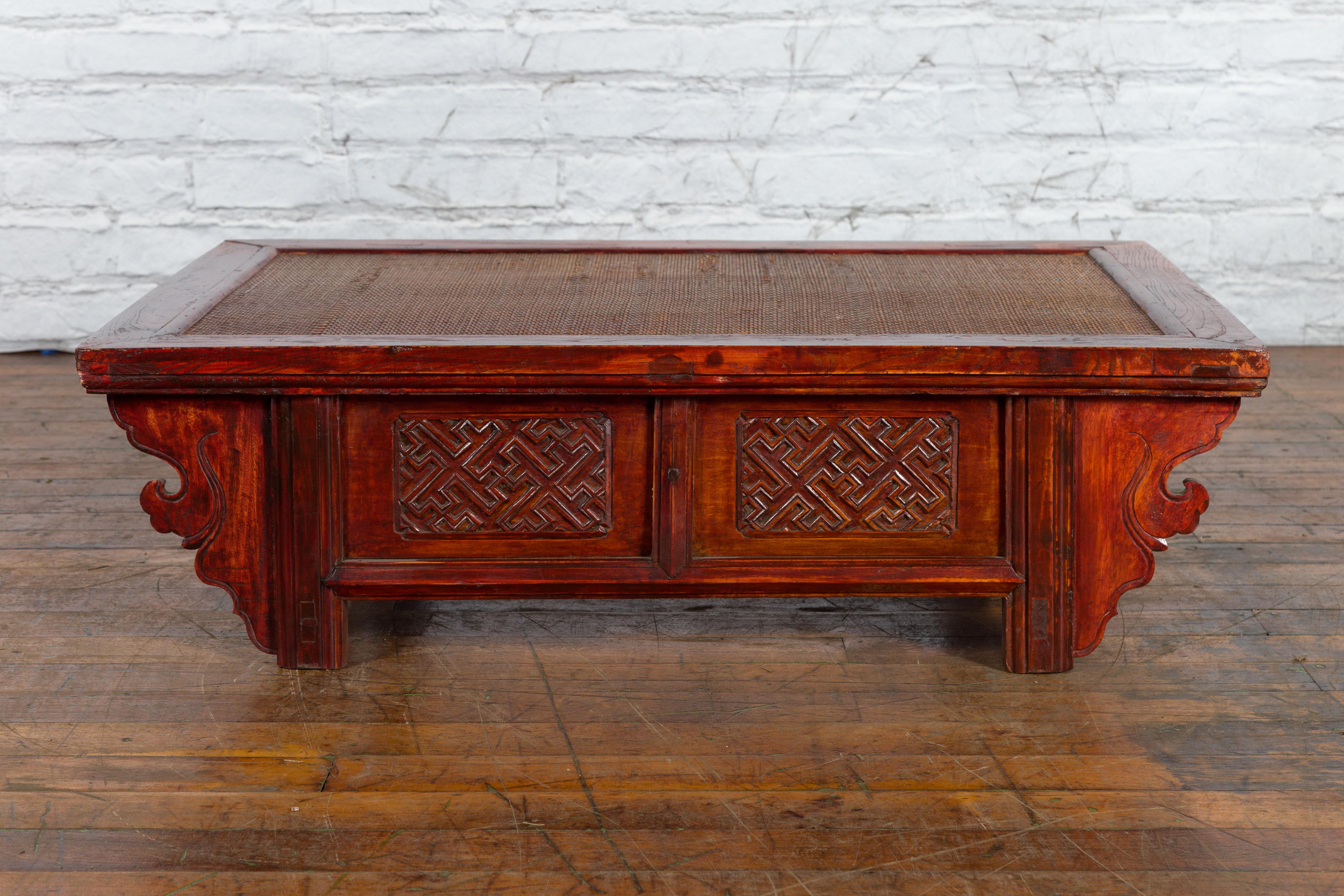 An antique Chinese Qing Dynasty period dark red lacquer wooden low coffee table from the 19th century, with rattan top, low-relief carved meander motifs and spandrels. Created in China during the Qing Dynasty in the 19th century, this low coffee