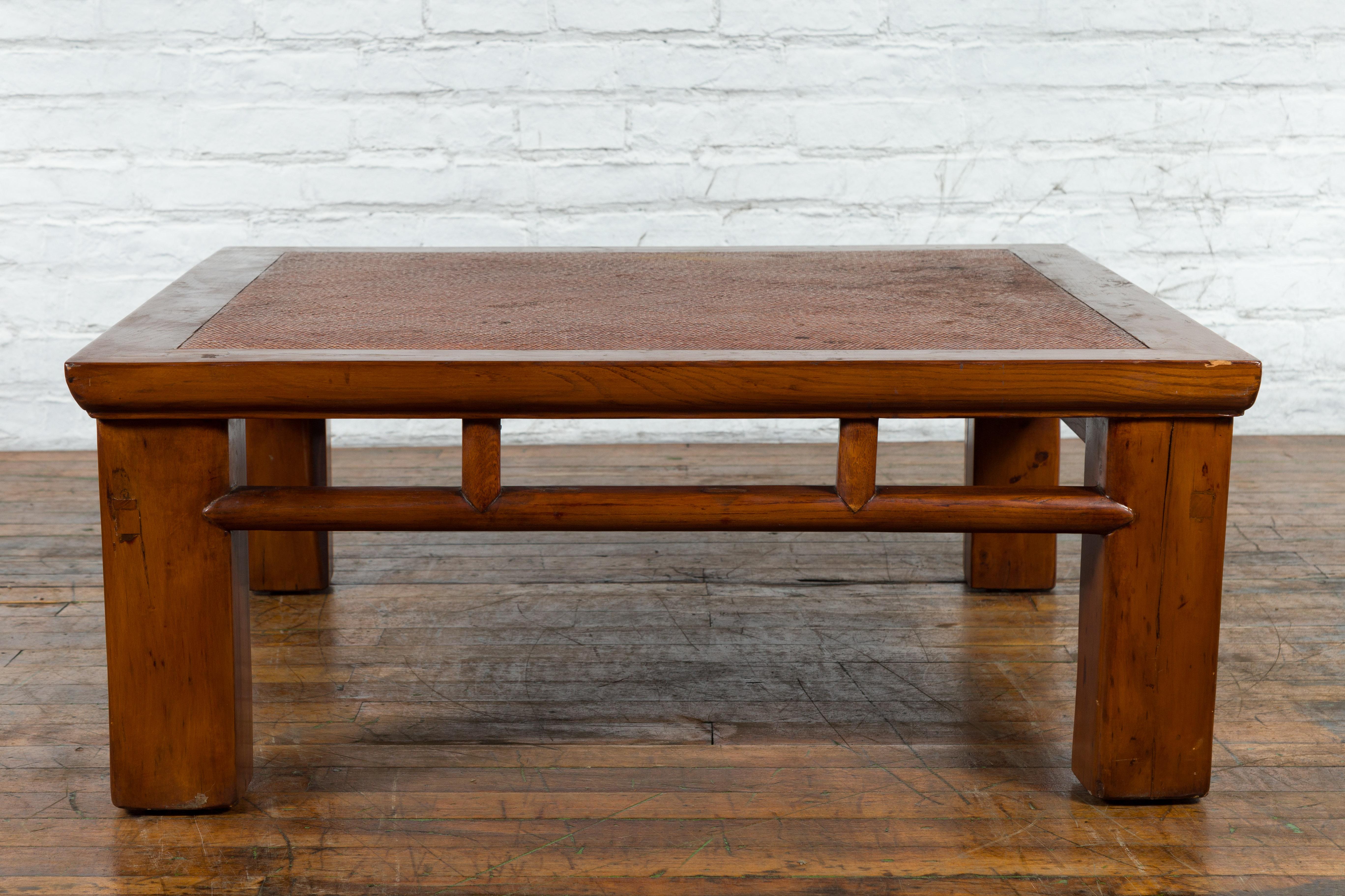 An antique Chinese Qing Dynasty period elm wood coffee table from the 19th century, with hand-woven rattan top inset, square legs, open apron and pillar strut motifs. Created in China, this low table was originally made from a cut down Lohan bed,