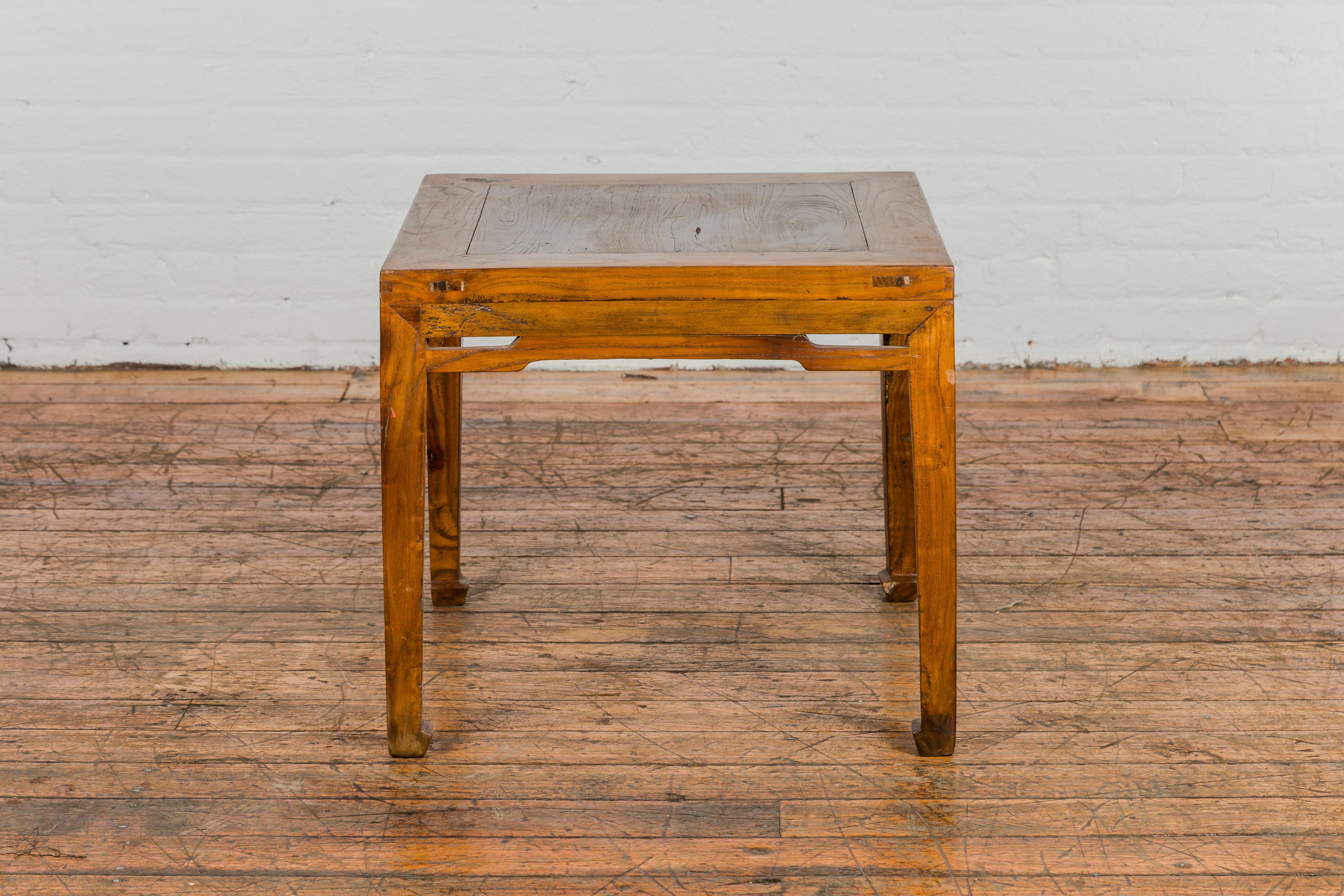 A late Qing Dynasty period elm side table from the early 20th century, with carved humpback stretcher apron, horse hoof feet and warm patina. Discover the enchanting allure of this late Qing Dynasty period elm side table, a masterpiece from the