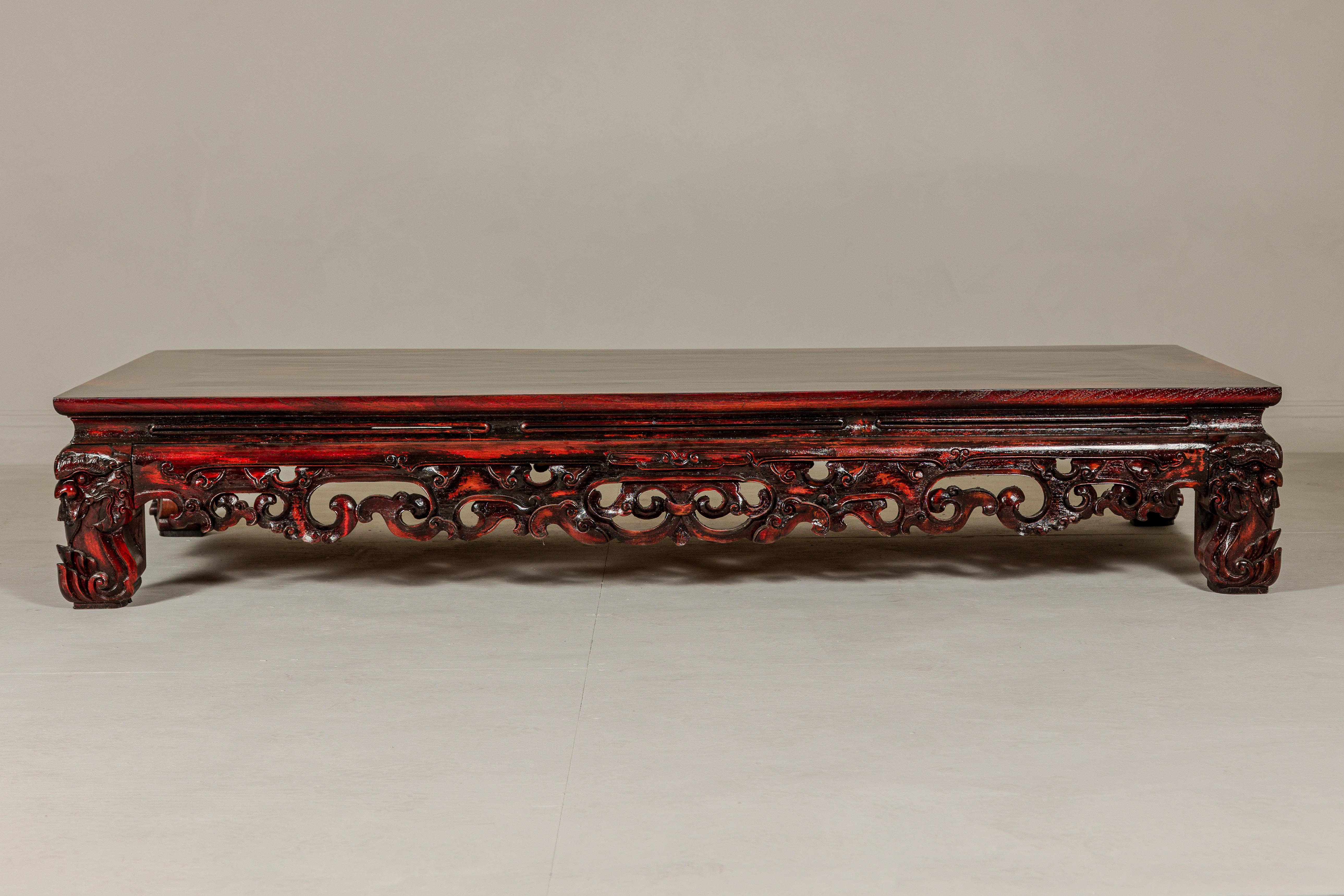 A Chinese Qing Dynasty long low Kang table from the 19th century with reddish brown lacquer and carved mythical motifs. This Chinese Qing Dynasty Kang table from the 19th century is a testament to the timeless allure of traditional craftsmanship.