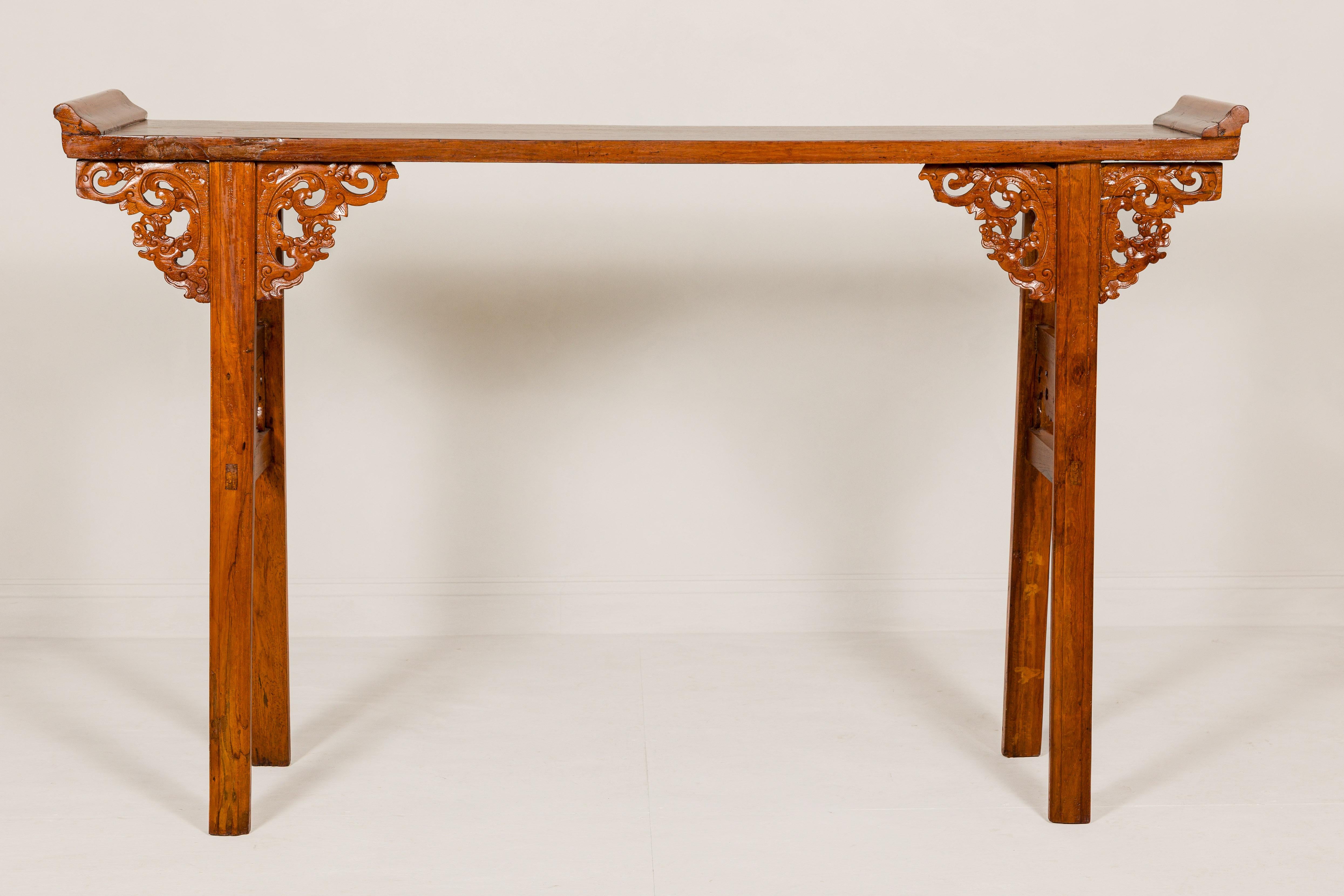 A Qing Dynasty period tall altar console table from the 19th century, with everted flanges, carved spandrels and double side supports. This magnificent Qing Dynasty period altar console table from the 19th century is a testament to the exquisite