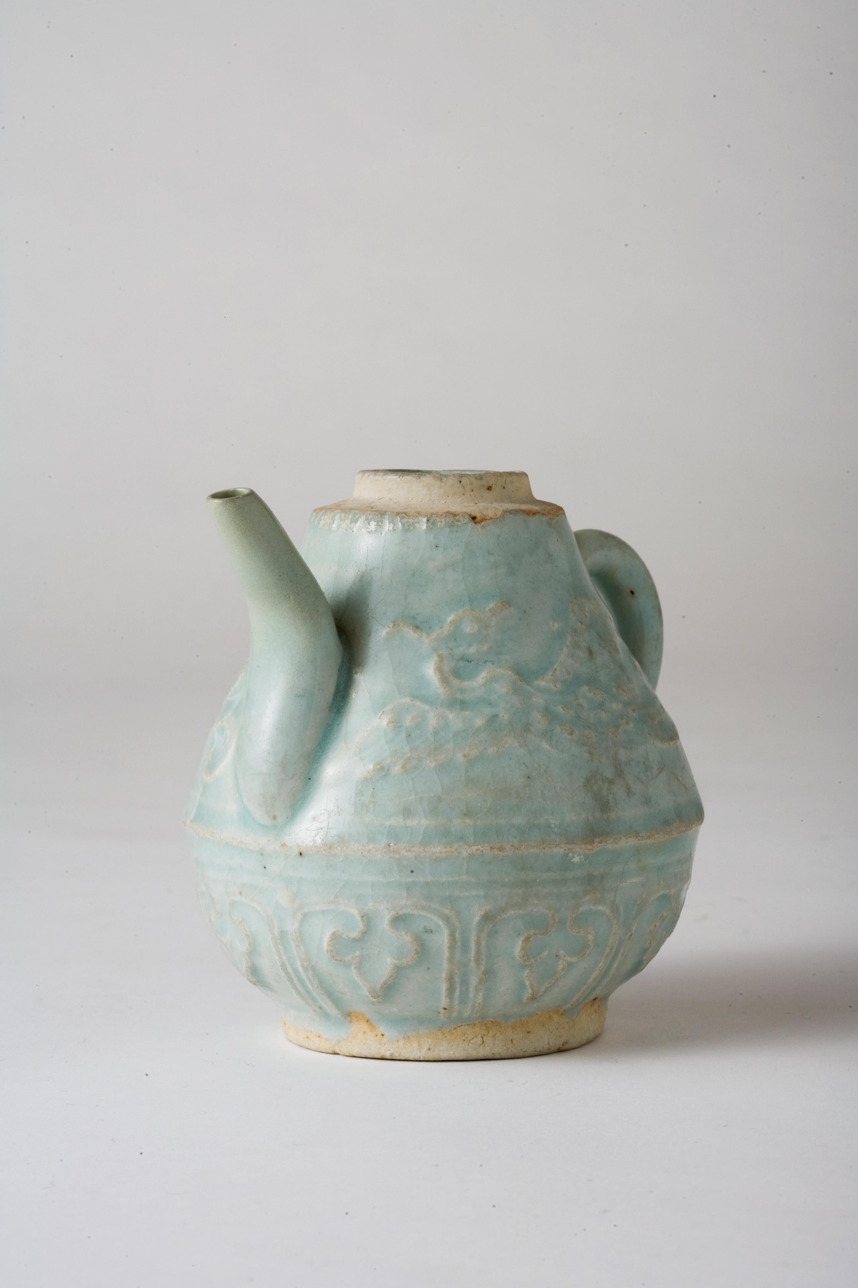 This small ewer is an exquisite example of Qingbai ware, known for its pale blue-tinged glaze. The vessel showcases the advanced ceramic techniques and artistic sophistication of the era. Its delicate form is enhanced by relief decorations depicting