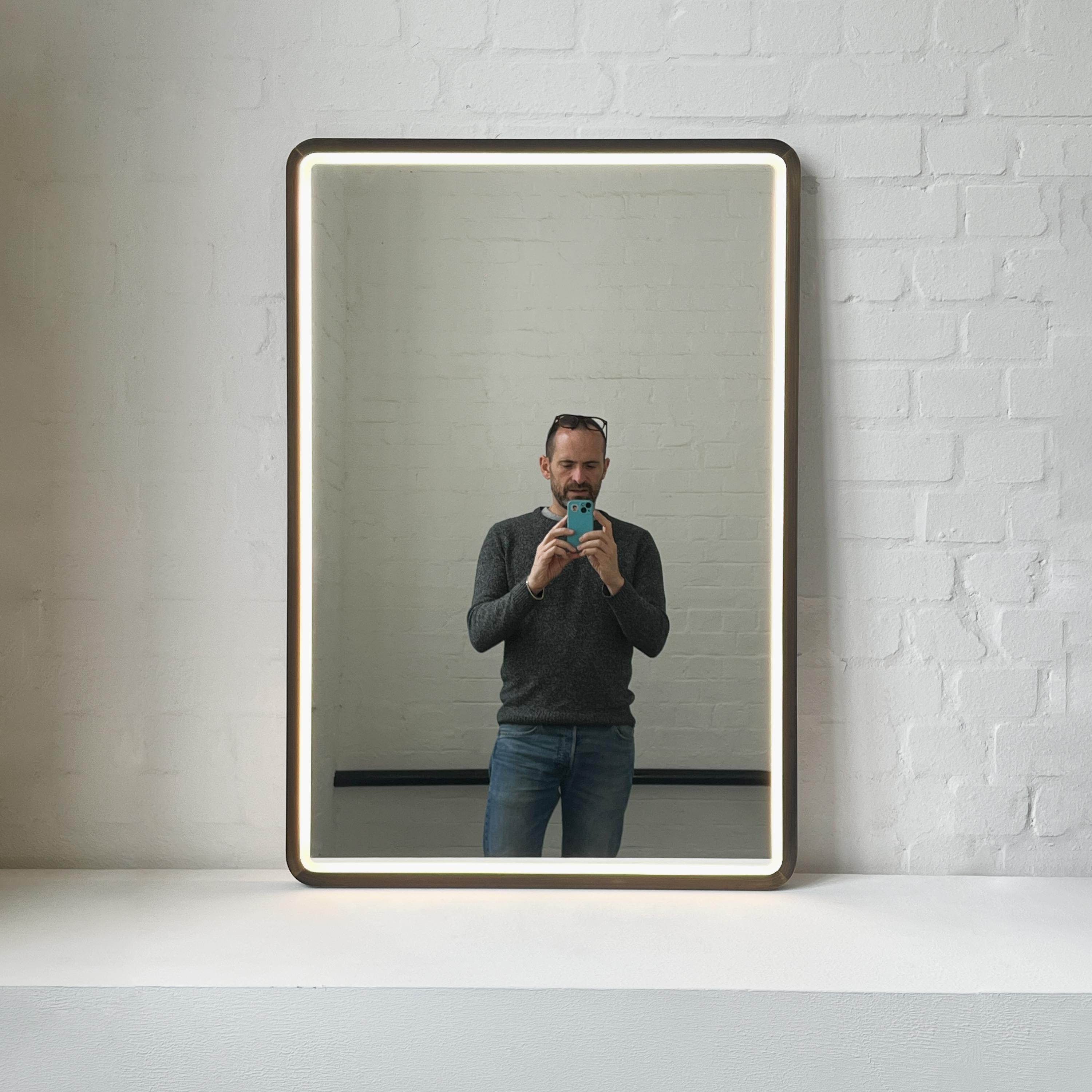 Handcrafted front illuminated rectangular mirror with mitred rounded edges and a bronze patina brass mitred full frame. Designed and handcrafted in London, UK. This mirror is fully customisable to suit the specific requirements of each