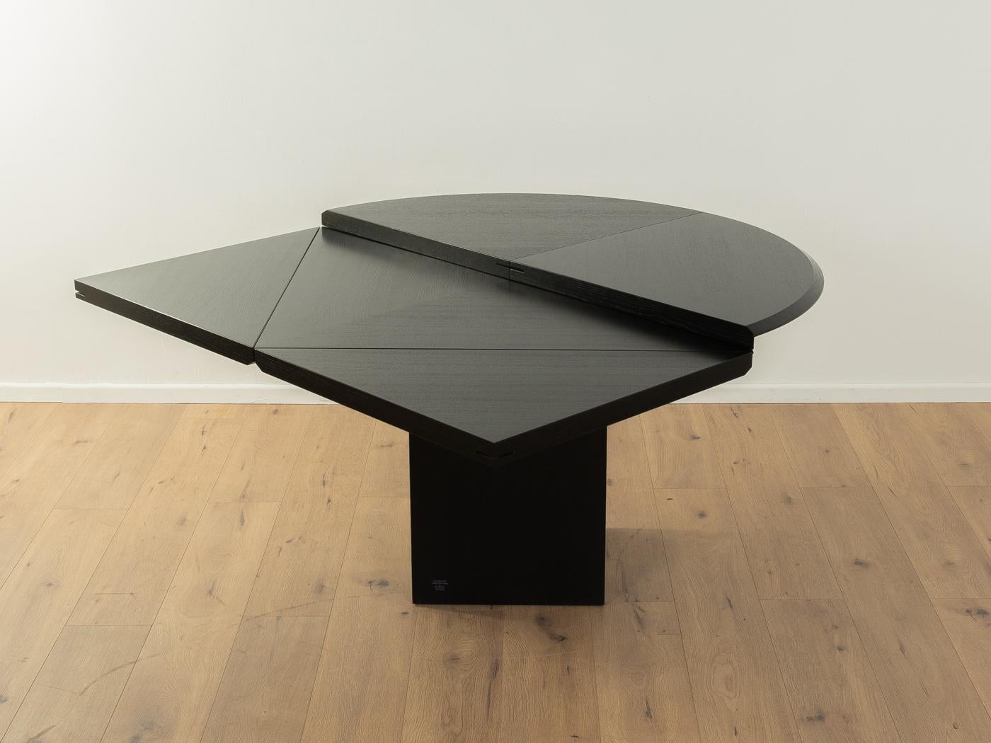 Quadrondo dining table from the 1980s by Erwin Nagel for Rosenthal Einrichtung. High-quality construction consisting of a squared base and a table top in black stained ash veneer. By unfolding each quarter, the round table top can be converted into