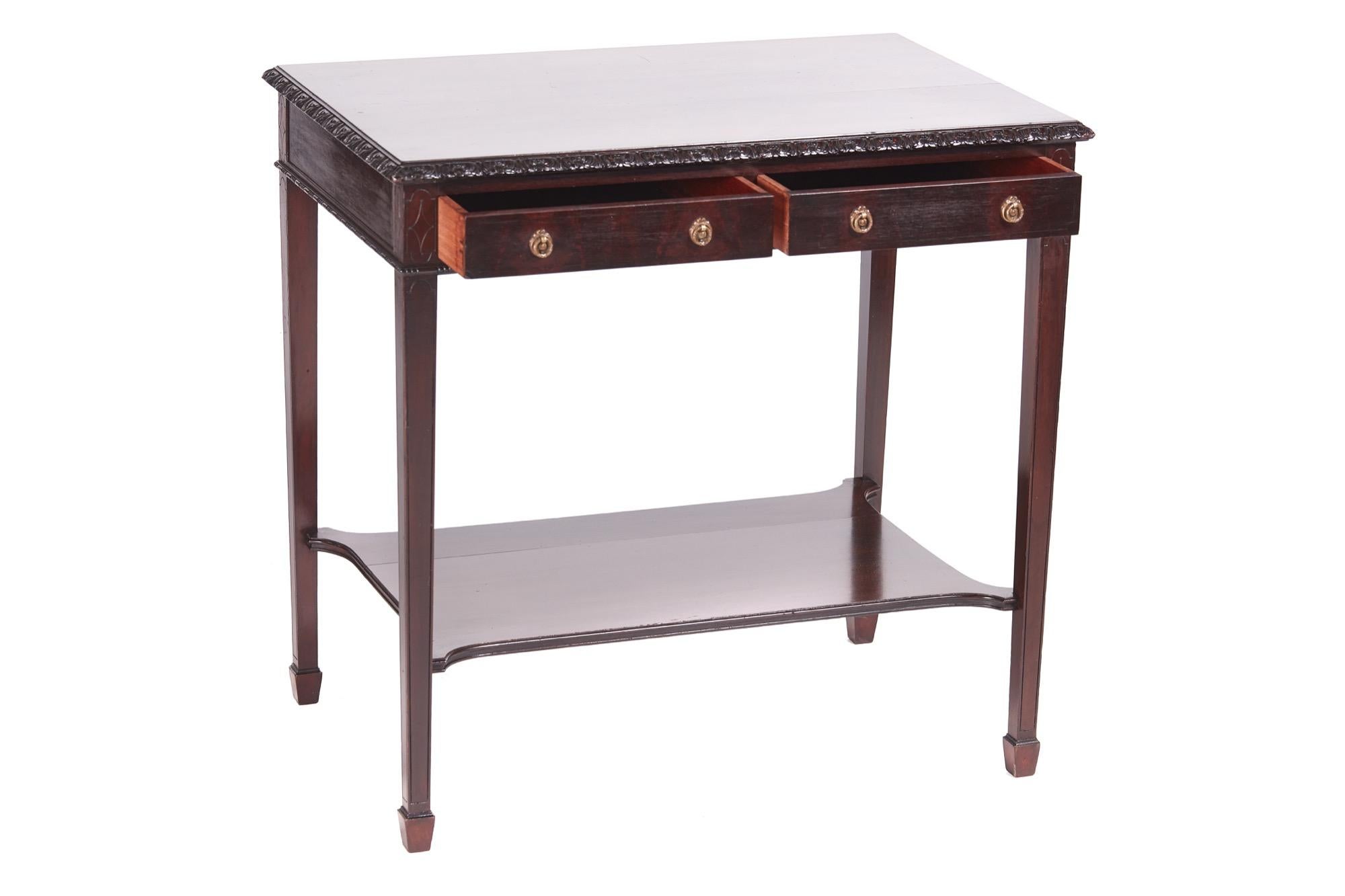 Quality Edwardian mahogany freestanding side / lamp table having a glorious mahogany top with a quality carved edge; two frieze drawers with original brass handles standing on four square tapering legs with spade feet united by a shaped