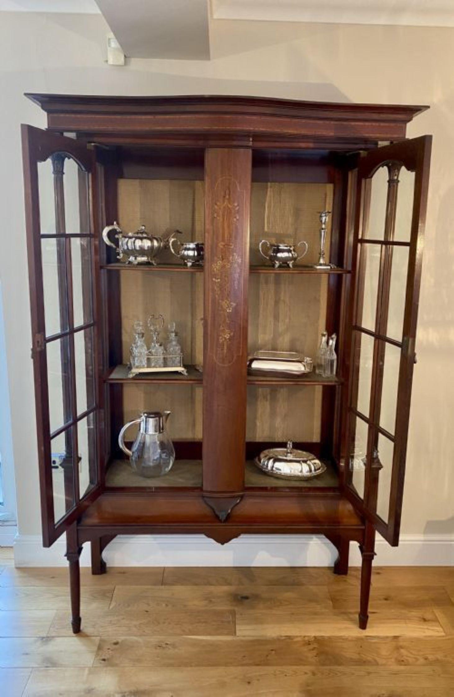 Quality antique Edwardian mahogany inlaid display cabinet having a quality inlaid serpentine shaped cornice above a fantastic marquetry inlaid center panel flanked by a pair of astral glazed doors opening to reveal tow display shelves, two superb