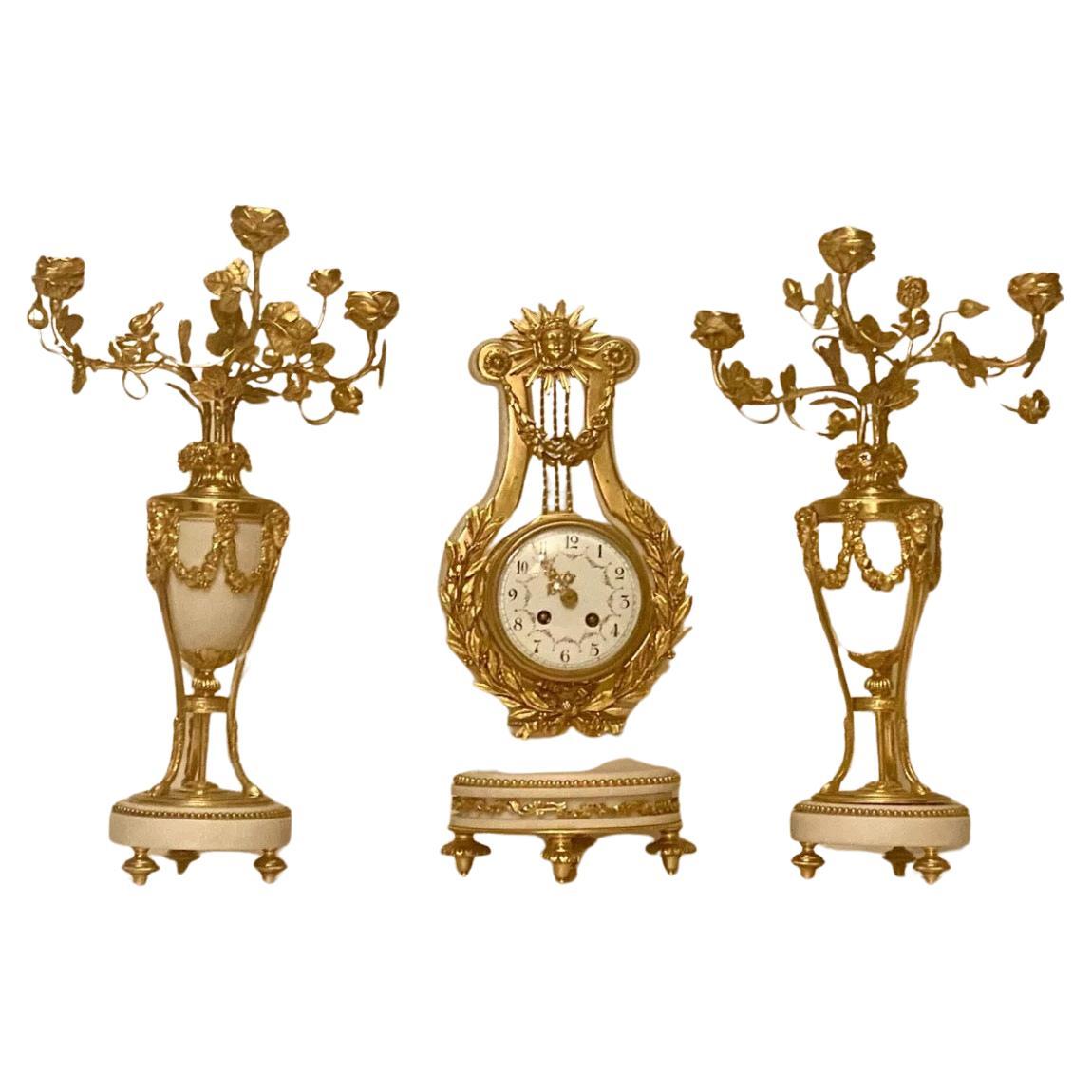 This stunning French clock set from the 19th century boasts a beautiful combination of marble and bronze materials, with intricate designs in white statuary colour.  
The clock comes with matching garnitures and is an original piece from Vincenti &