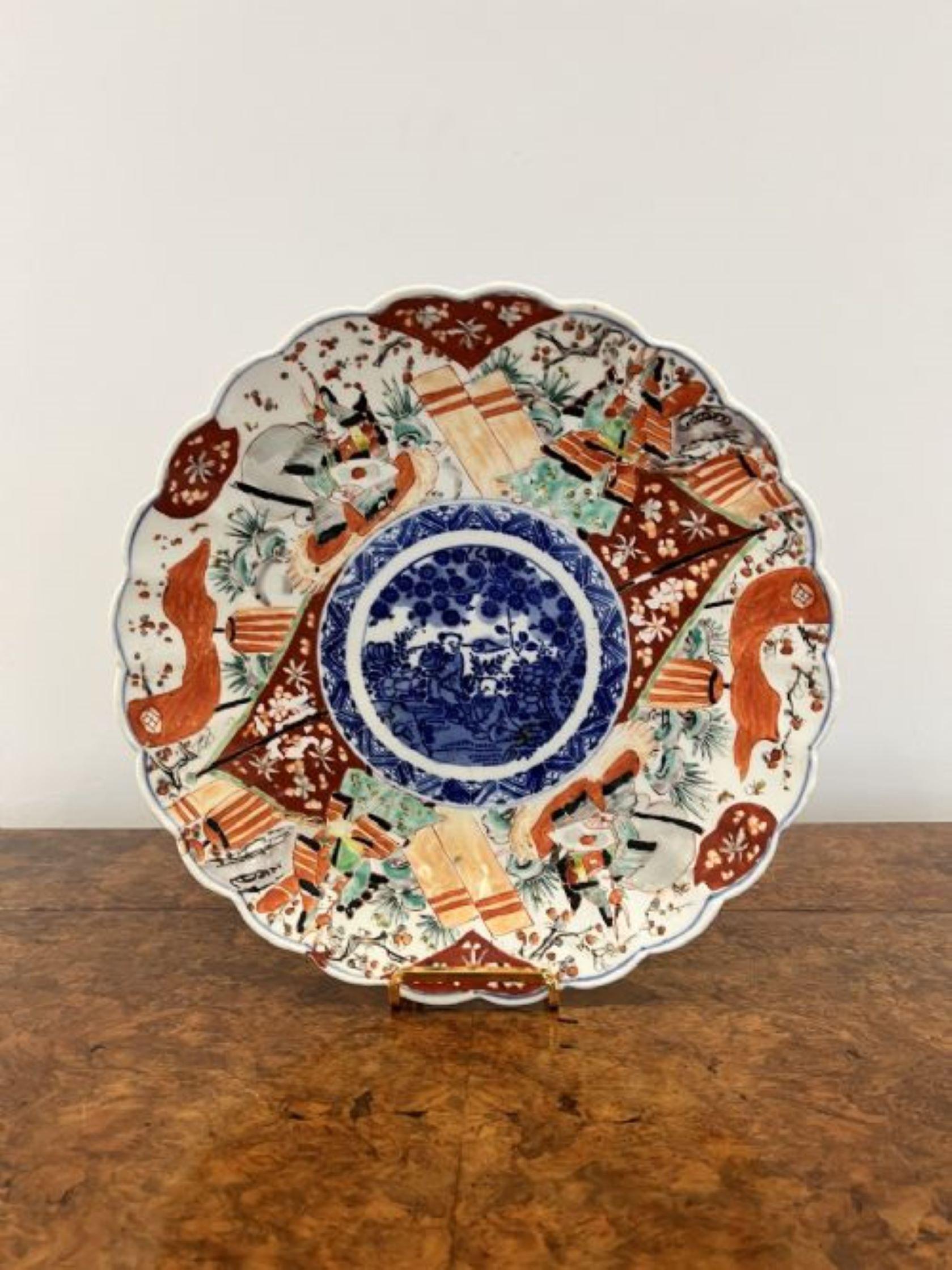 Quality antique Japanese imari plate having a quality antique imari plate with a scalloped shaped edge with hand painted panels with flowers, leaves, trees and people in vibrant red, blue, green, white and black colours, to the centre a hand painted