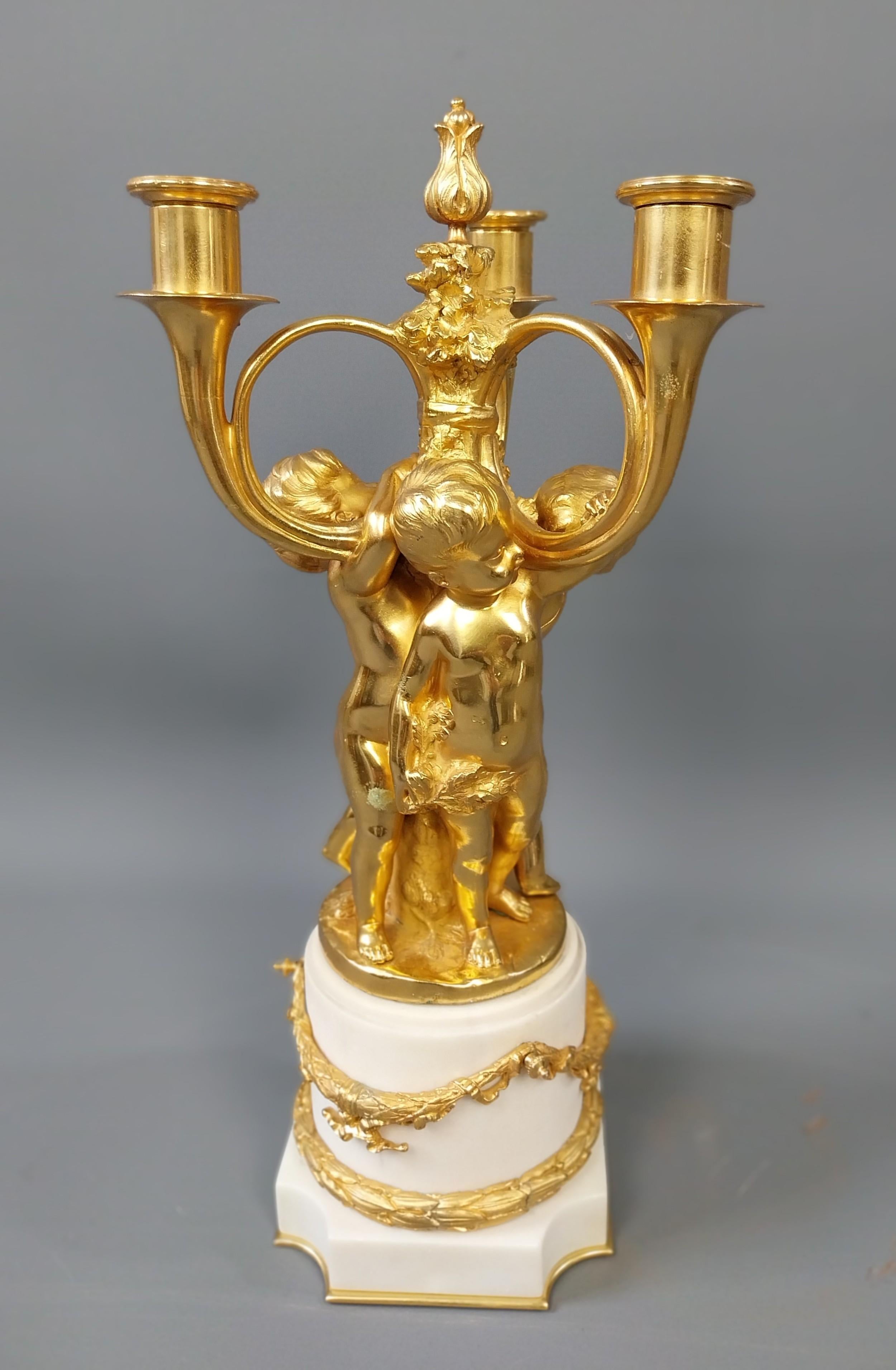 Candelabro in bronzo dorato con la forma di tre cherubini appoggiati a un ceppo d'albero frondoso, ognuno dei quali regge un'ampia candela unita da un centro di foglie naturalistiche rifinito con un finale. I cherubini poggiano su una bella base di