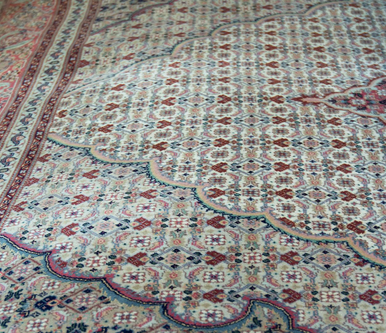 
This vintage, circa 1970, Tabriz rug has an ivory field with dense rust-red and shaded buff-brown and blue herati-pattern around a central similar shaded red and ivory cusped medallion with palmette pendants, the ivory and buff-brown spandrels