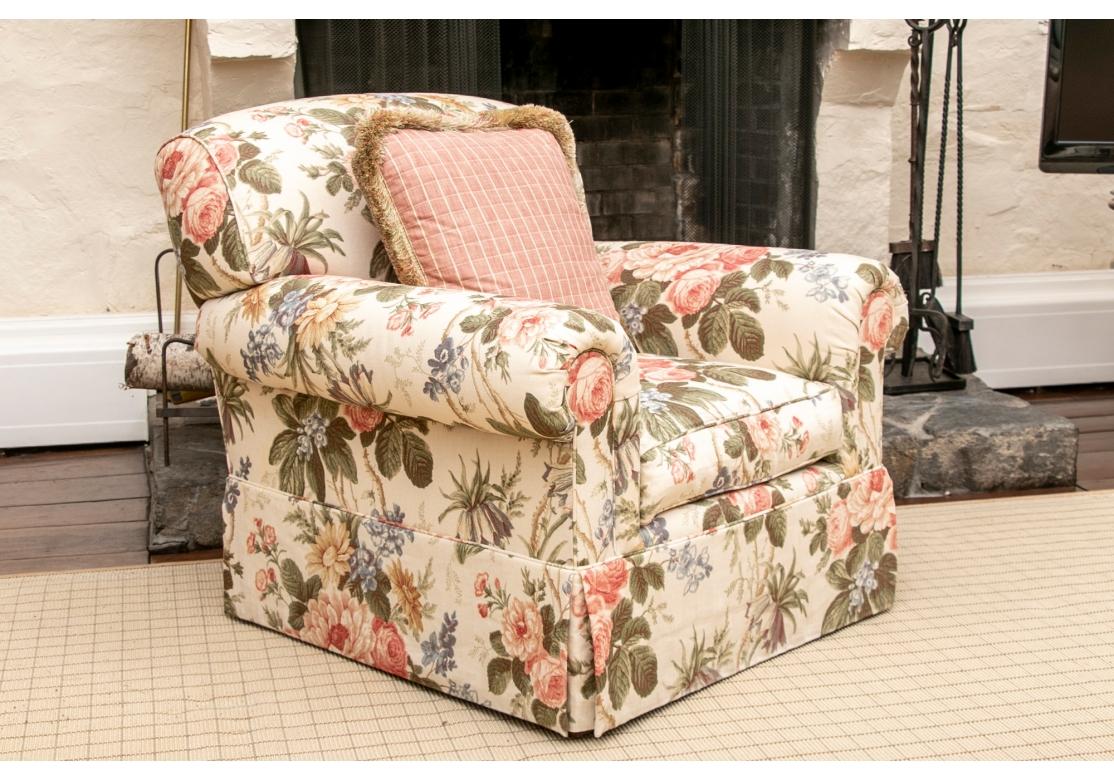 A classic club chair with sloping rolled back and rolled arms. The dark brown wood legs covered with a tailored skirt in the fine pastel floral print linen upholstery fabric. Along with a coordinating pink plaid fringed pillow. 
H. 36